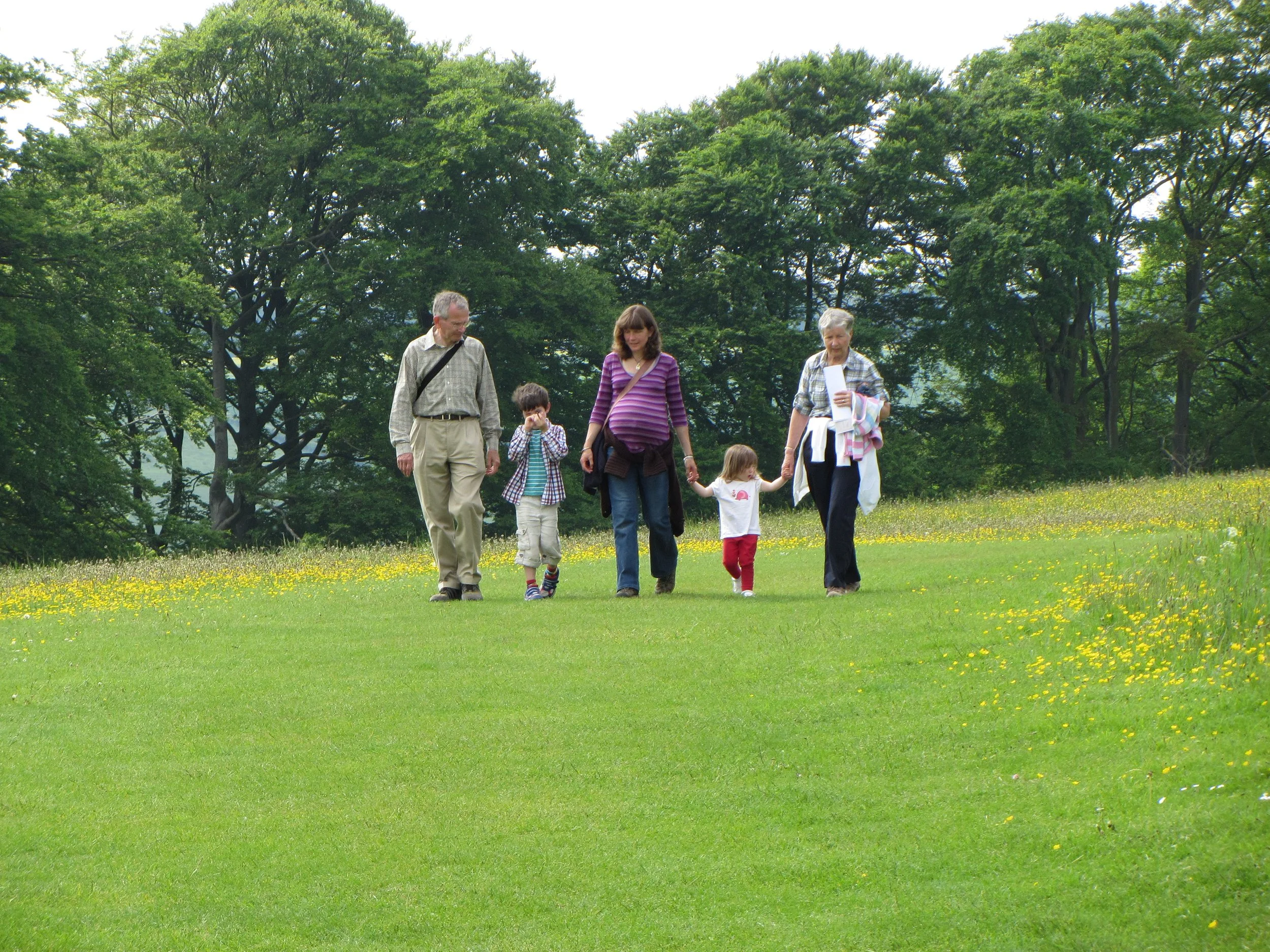 Pregnant woman walking through field with two children and their grandparents, trees in background.