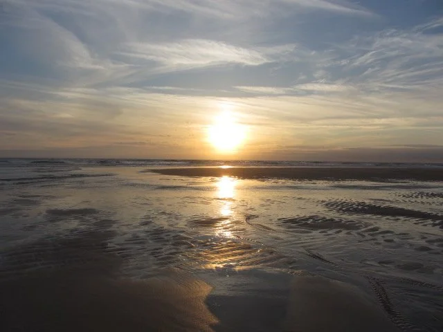 Sunset and wispy clouds over the sea, reflected in the water on the rippled sand