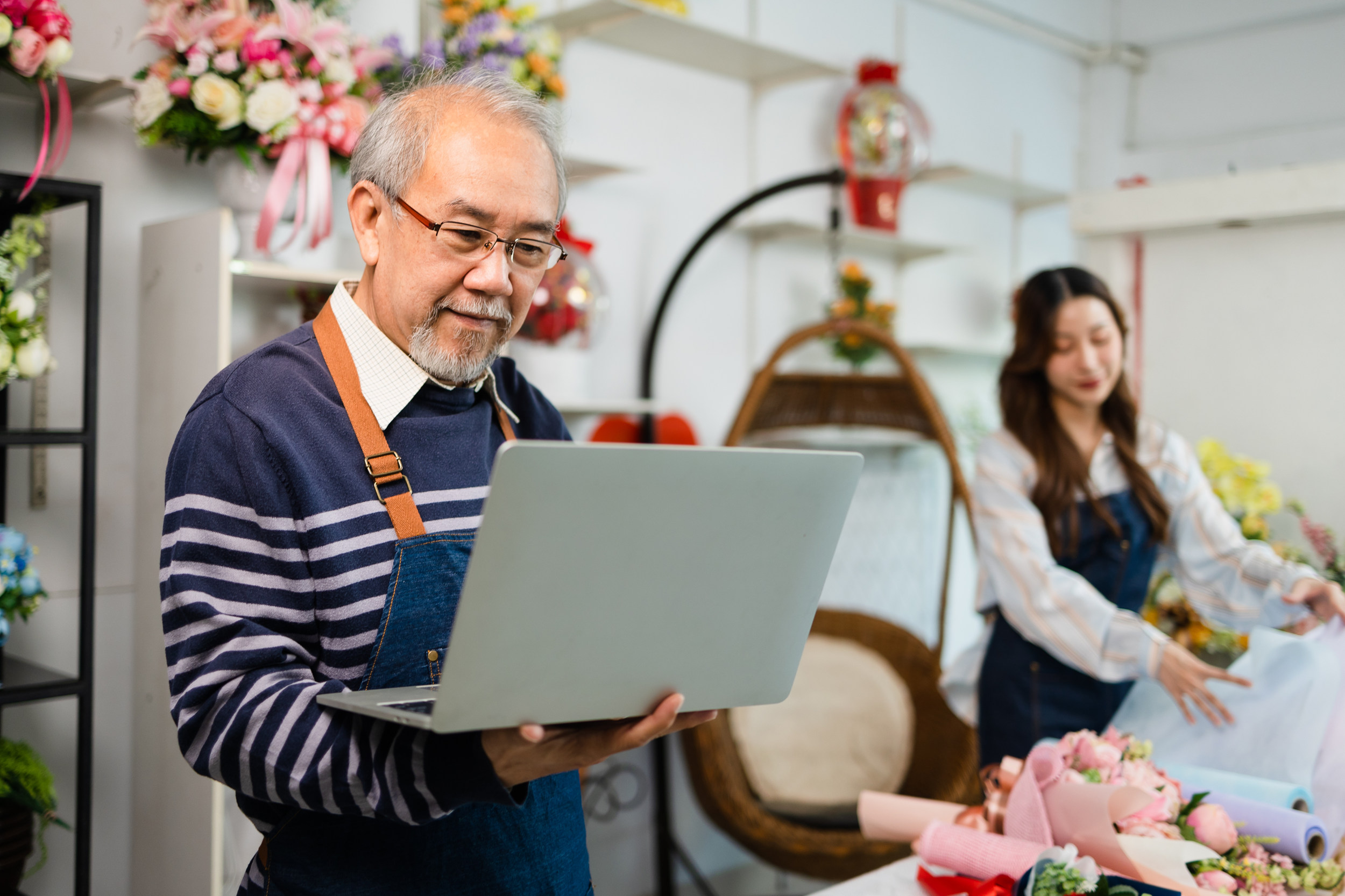 Portrait of mature male small business owner using laptop and looking at camera in flower shop