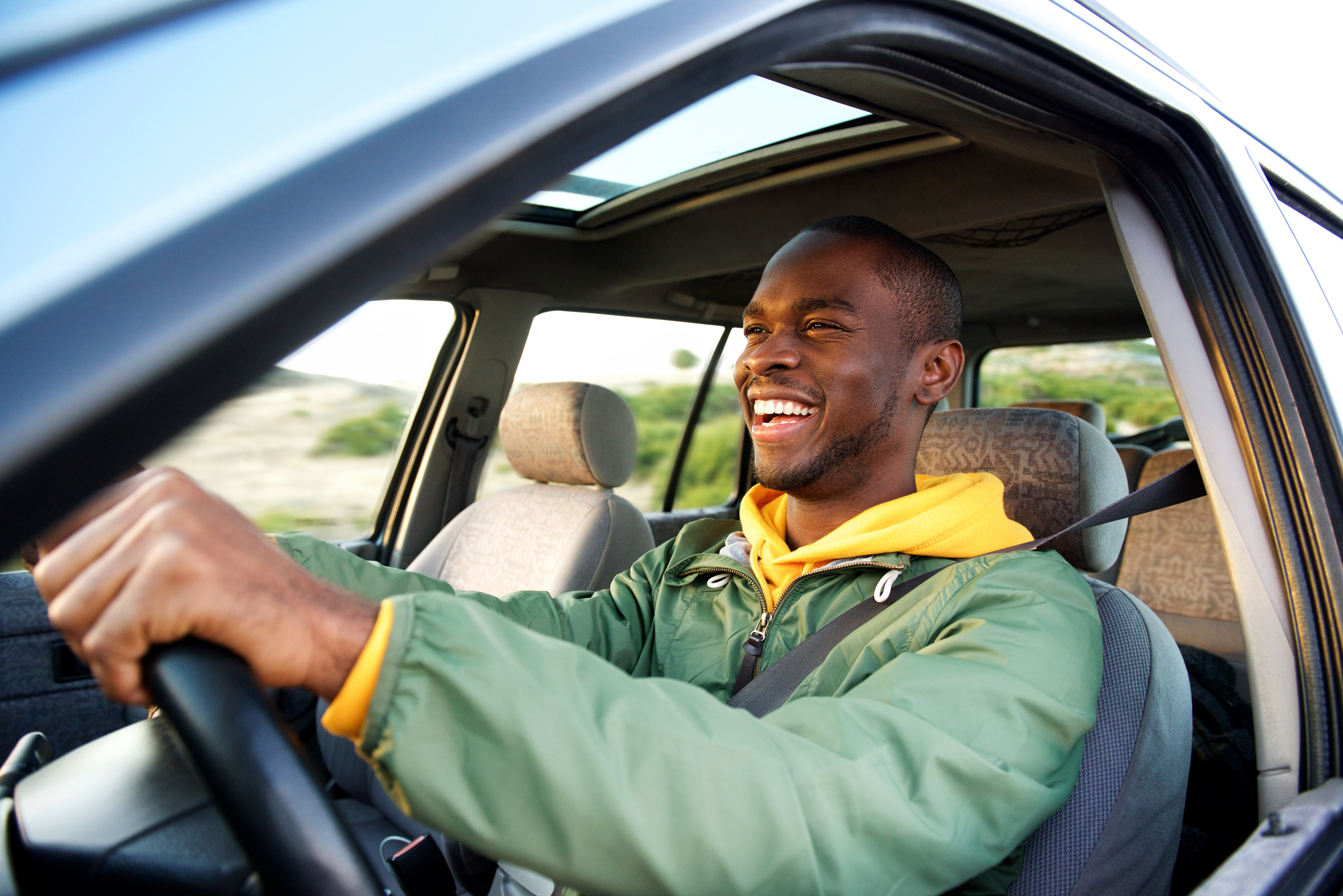 Side of happy black man driving his car in a green jacket