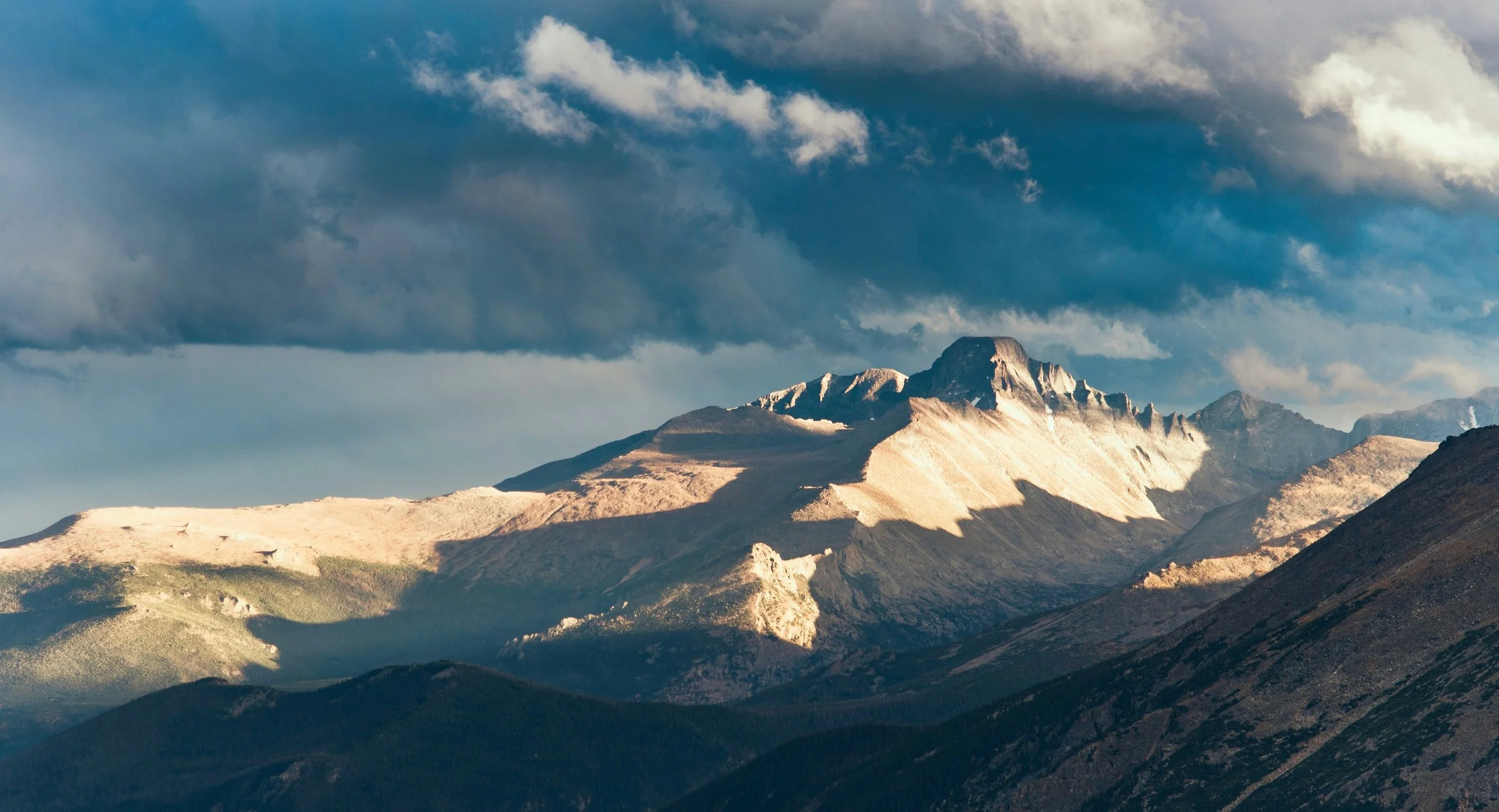 A mountain range under a partly cloudy sky with sunlight illuminating the peaks.
