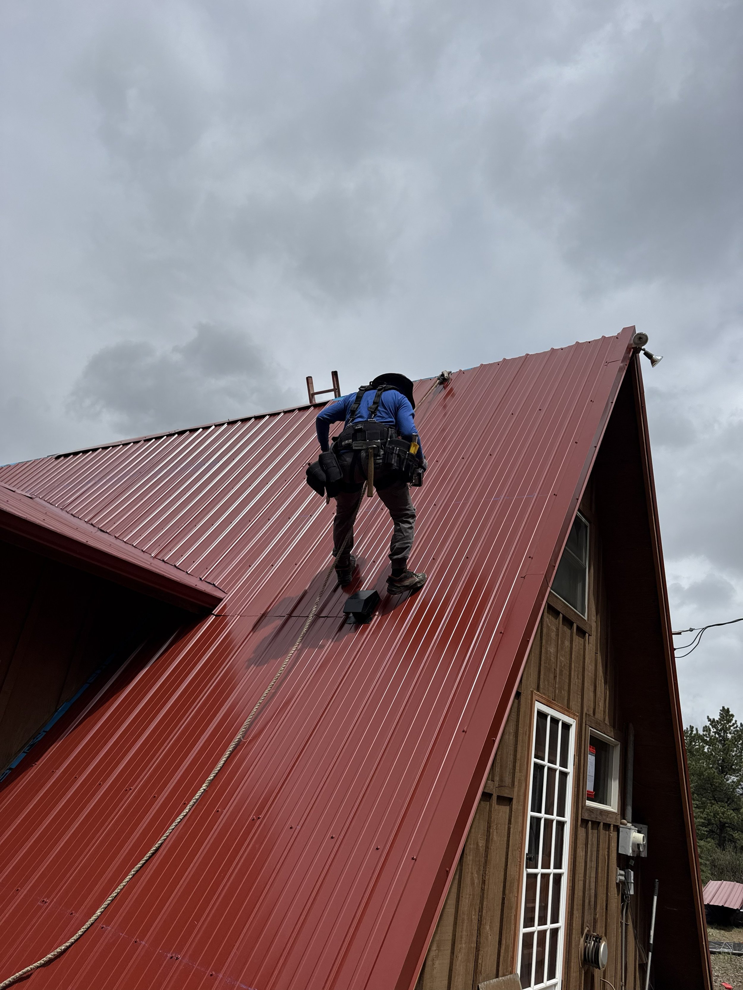 A Man following OSHA regulations works on a very steep metal roof in Colorado