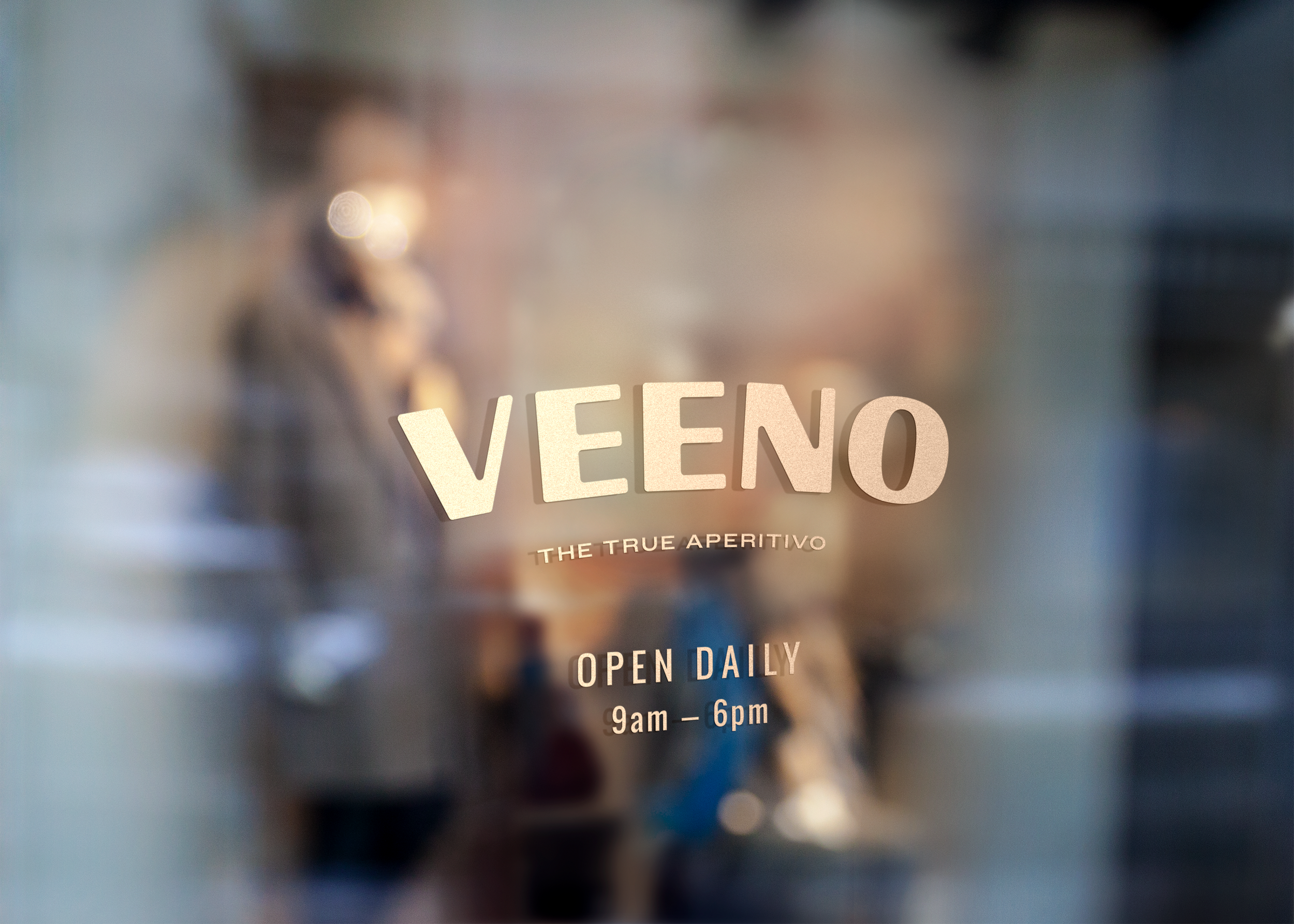 Close-up of a glass door with the restaurant name 'VEEO' and the tagline 'The True Aperitivo' written on the glass, along with opening hours 'Open Daily 9am - 6pm'; background is blurred.