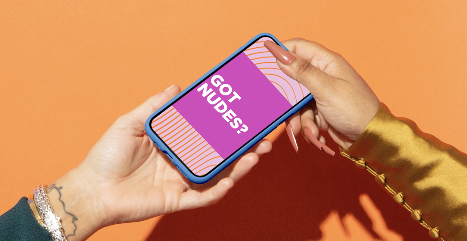 A person holding a smartphone with a pink and purple screen that reads 'GOT NUDESS?' against an orange background.