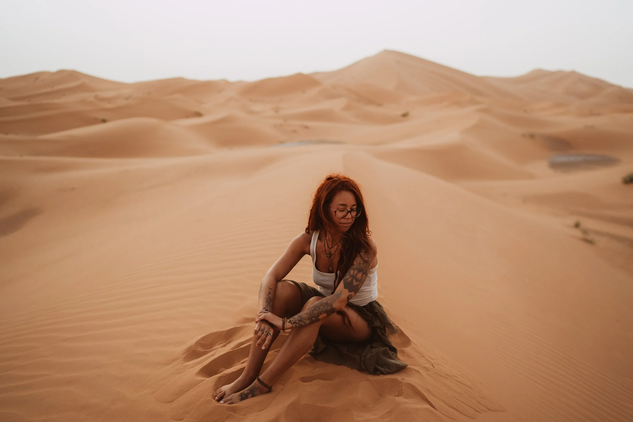 A woman with red hair, glasses, and tattoos, travelling, exploring the world.