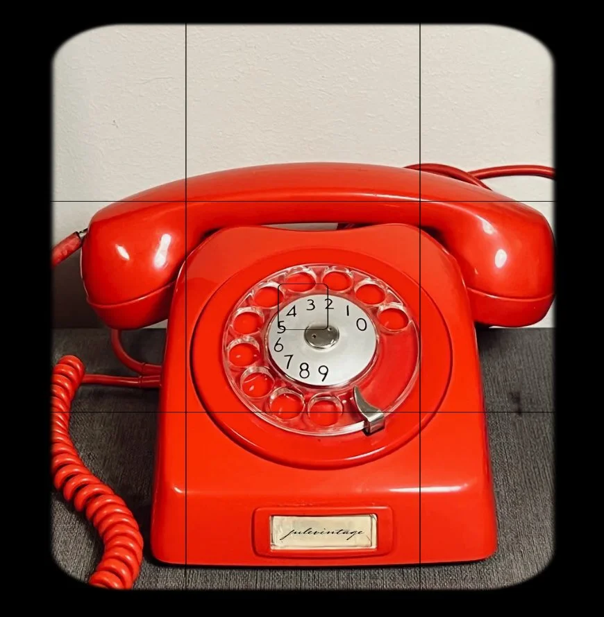 A vintage red rotary telephone with a circular dial and a coiled cord.