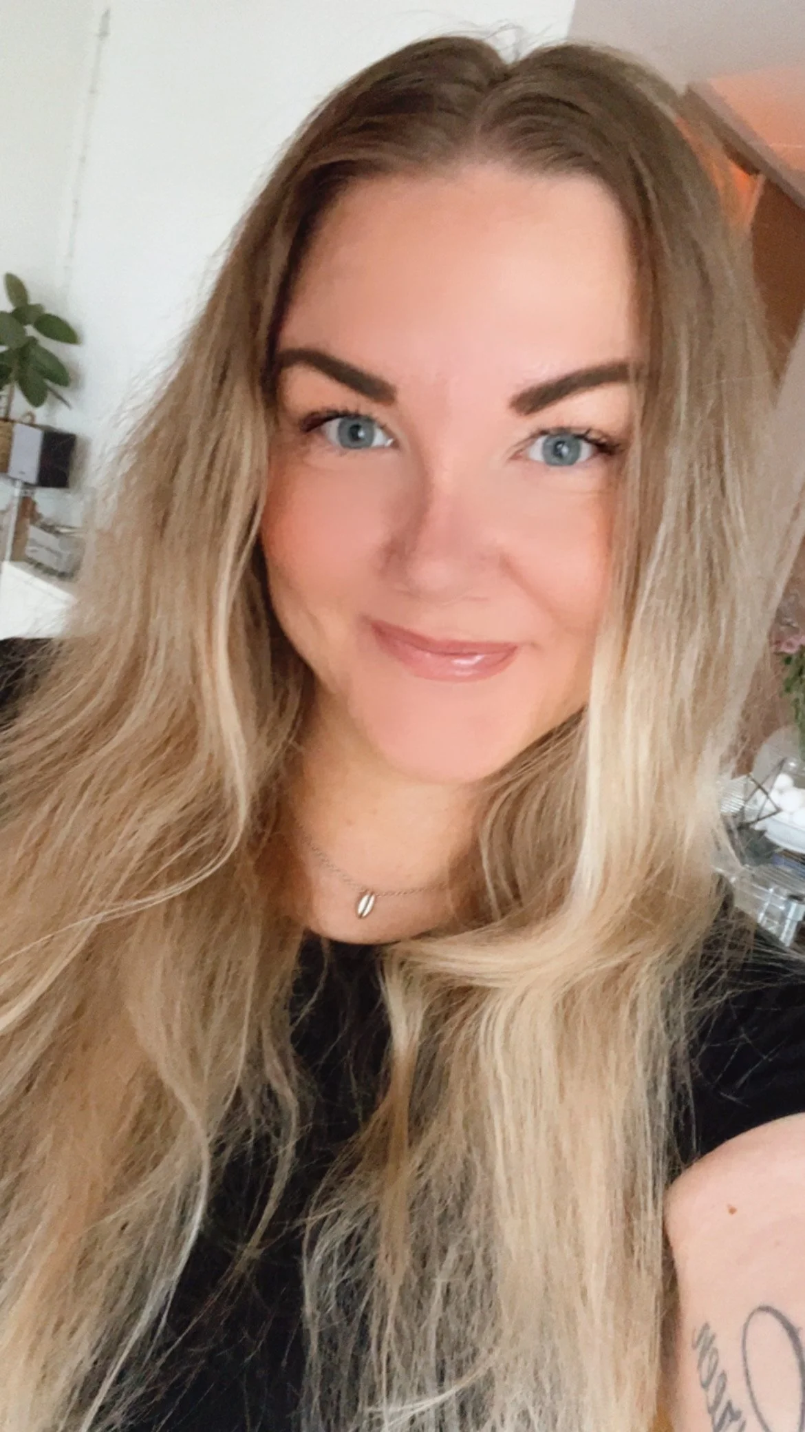 En kvinna med långt blont hår och blå ögon, ler, i ett inomhusmiljö