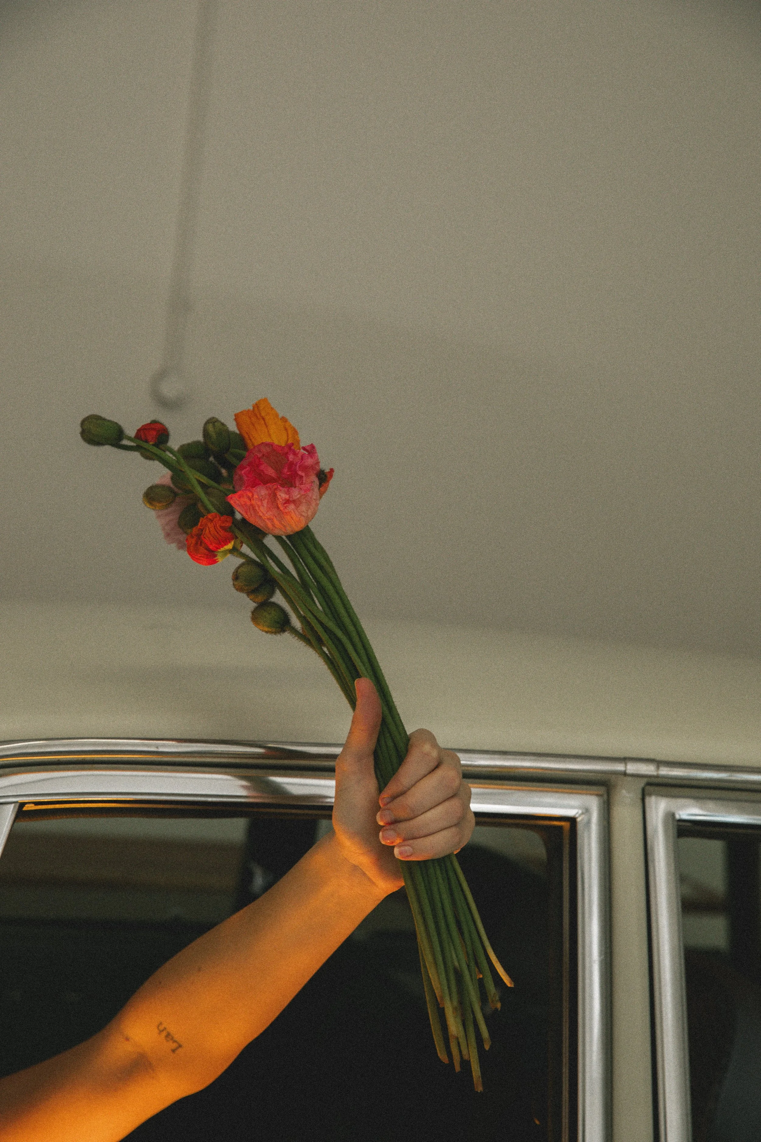 En hand håller ett vackert blombud med färgglada blommor framför ett bilfönster.