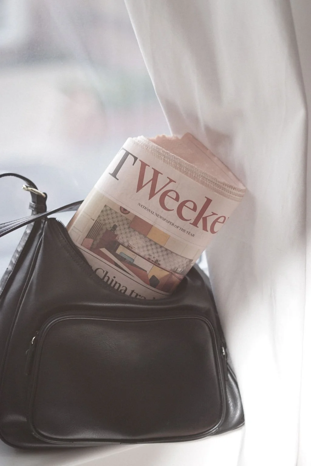 En svart väska med en veckad tidning som heter T Weke stickande ut ur en av fackarna.