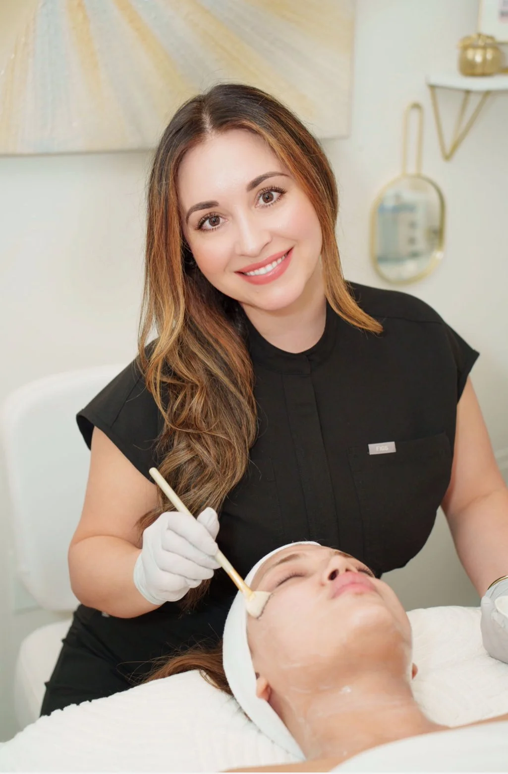 A woman receiving a facial treatment from a cosmetologist in a spa or clinic setting.
