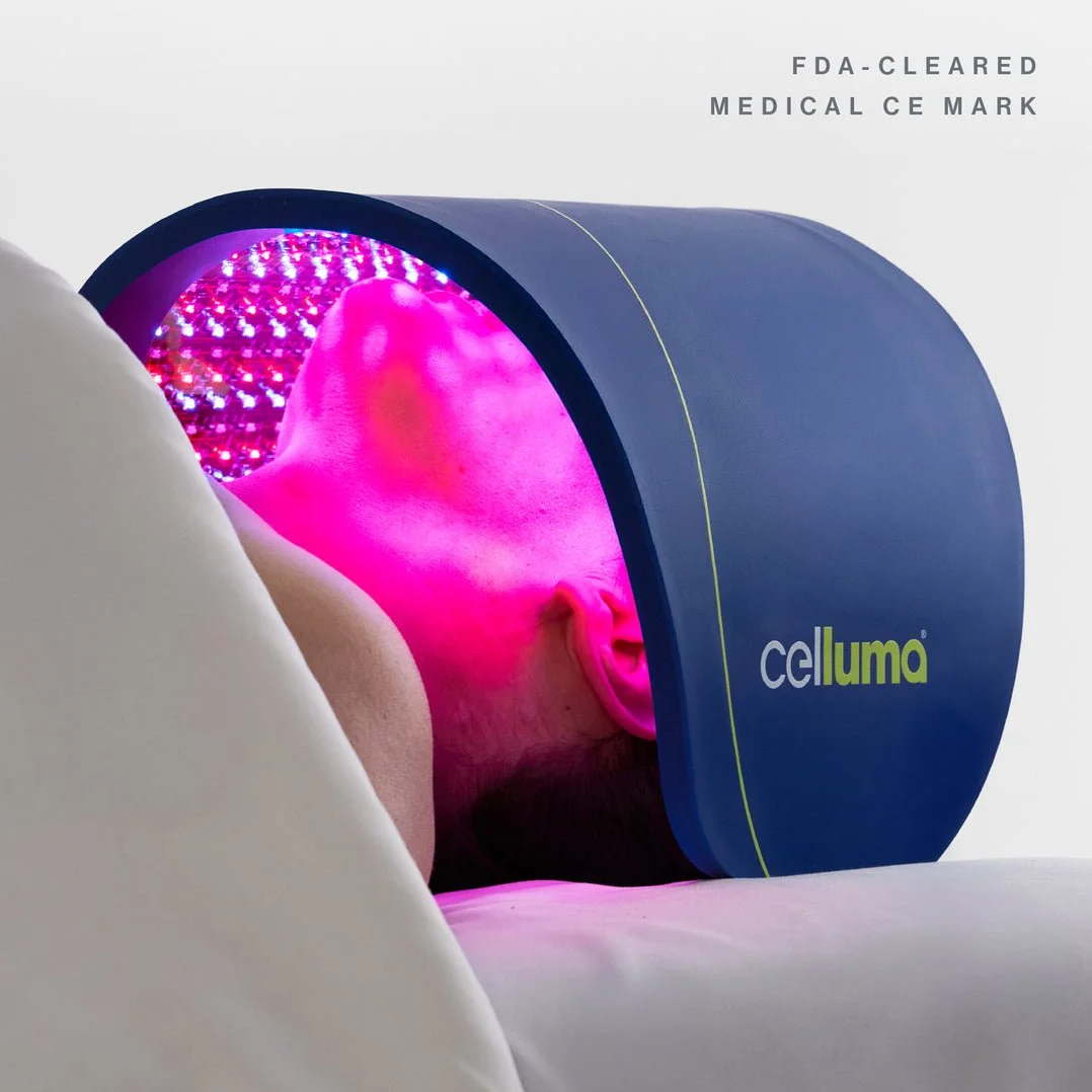 A woman receiving a red light therapy treatment in a medical spa or clinic, lying on a treatment bed with protective goggles on.