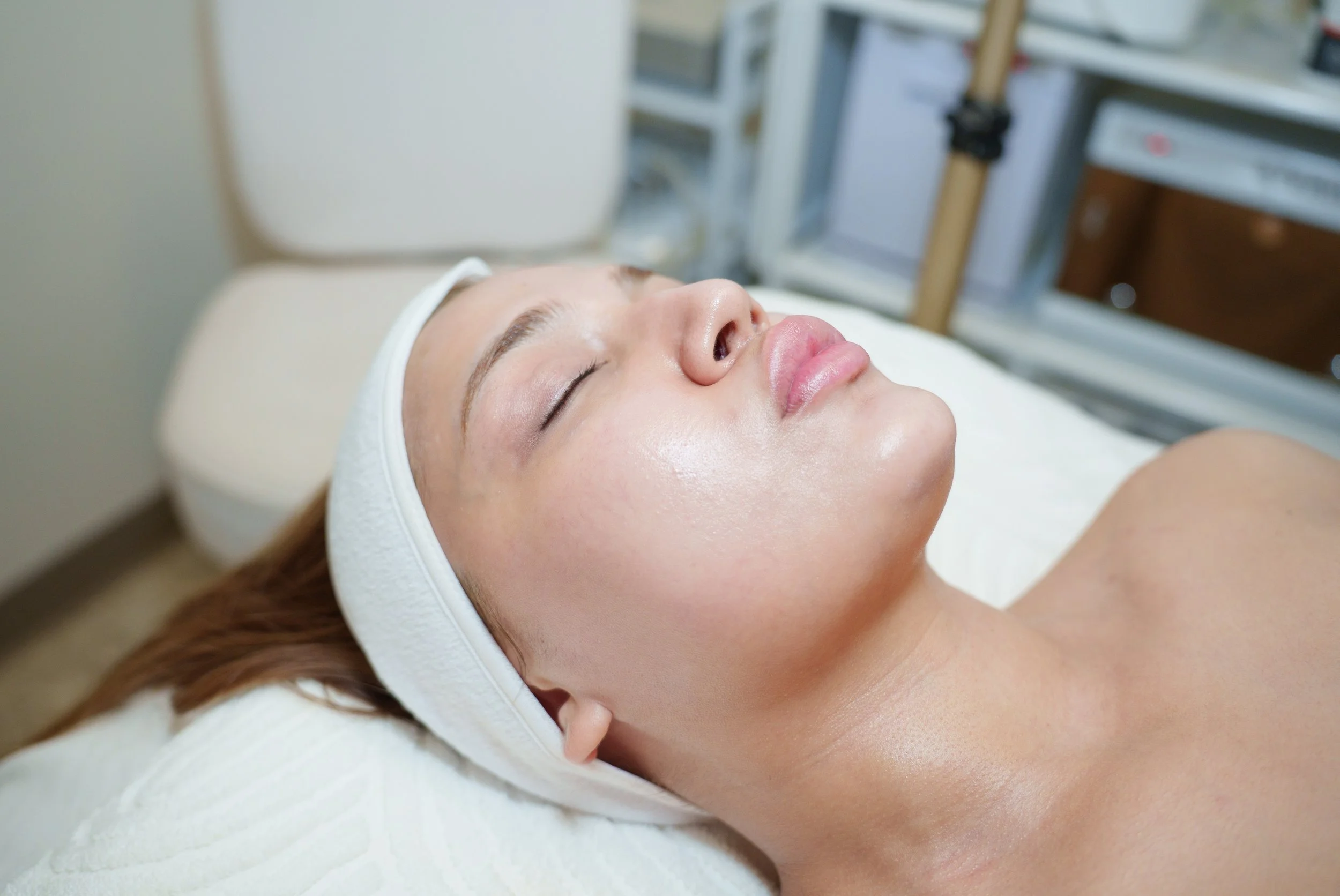 A woman receiving a facial treatment from an esthetician in a spa or clinic setting.