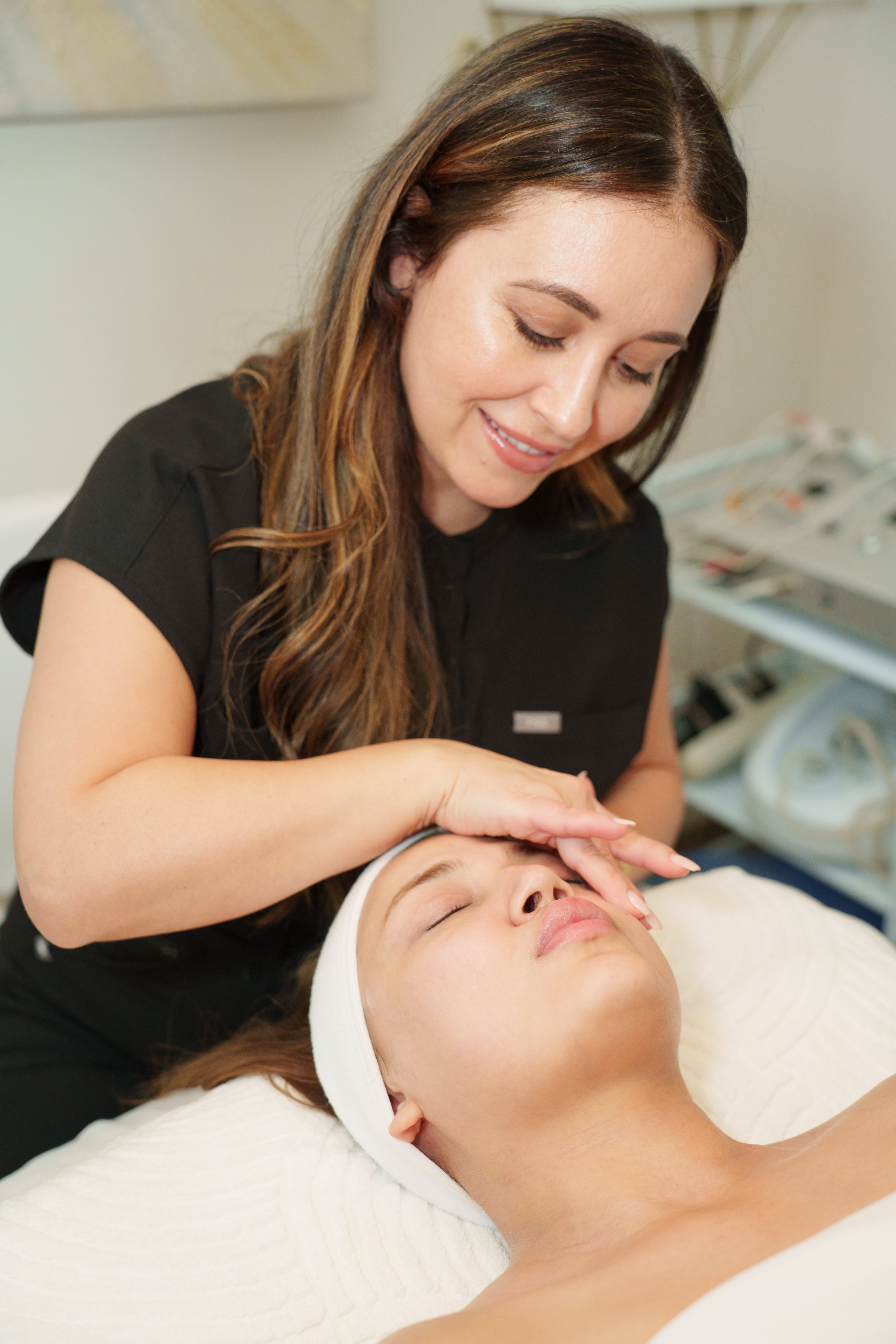 A woman receiving a facial treatment from an esthetician in a spa or clinic setting.