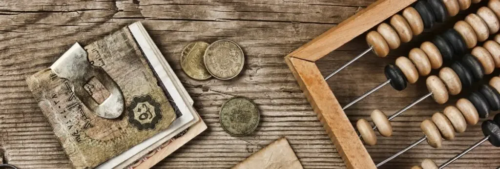A wooden table with Japanese yen bills and coins, a wooden abacus with black and natural beads.