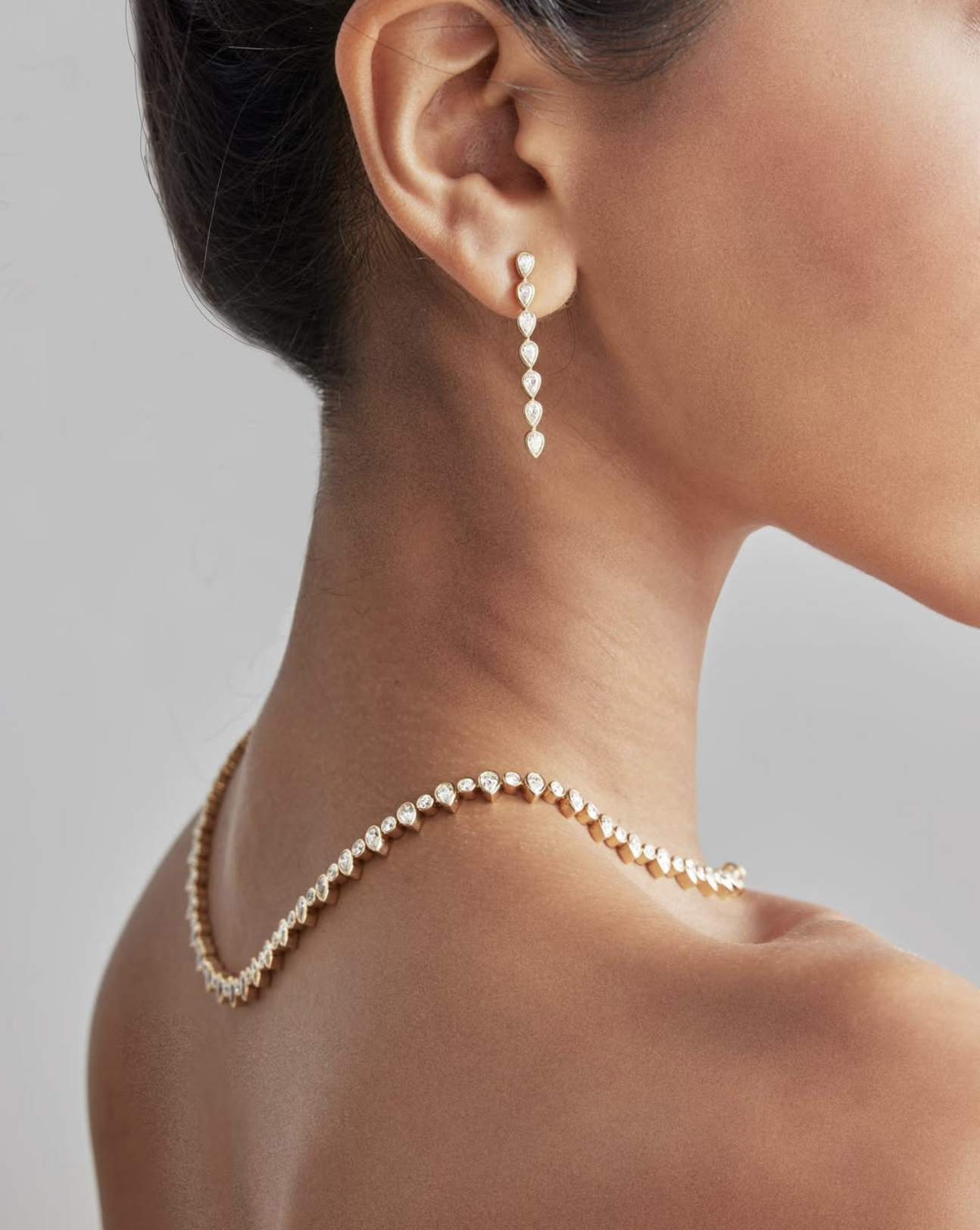 Close-up of a woman wearing diamond jewelry, including a dangling earring and a pearl necklace.