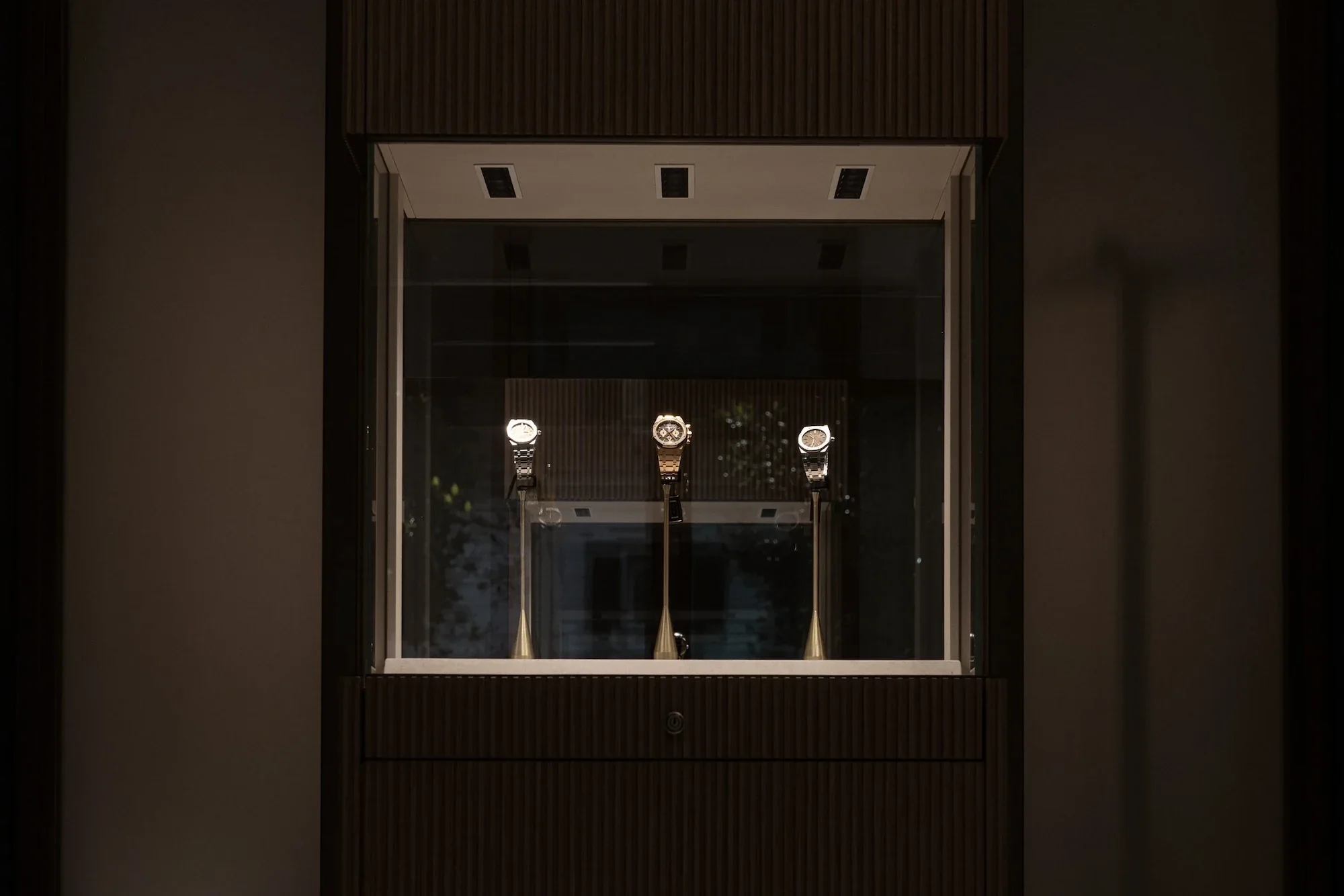 Display case with three luxury watches on stands in a well-lit, modern showroom or store.