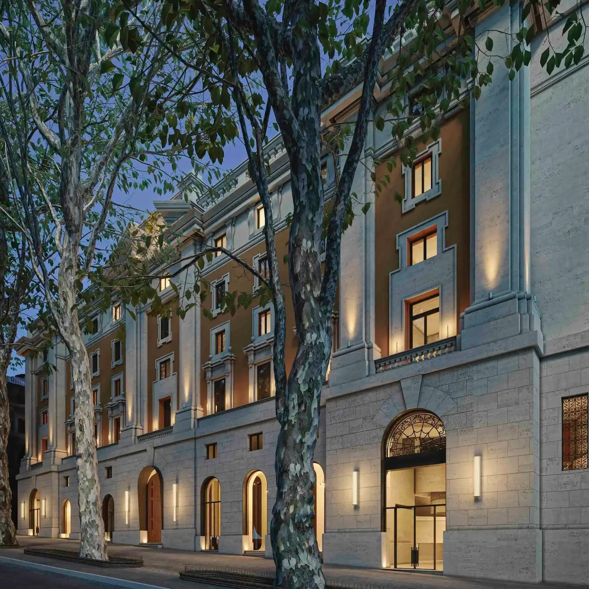 A multi-story building with lit windows at dusk, partially obscured by tall trees with peeling bark and green leaves.