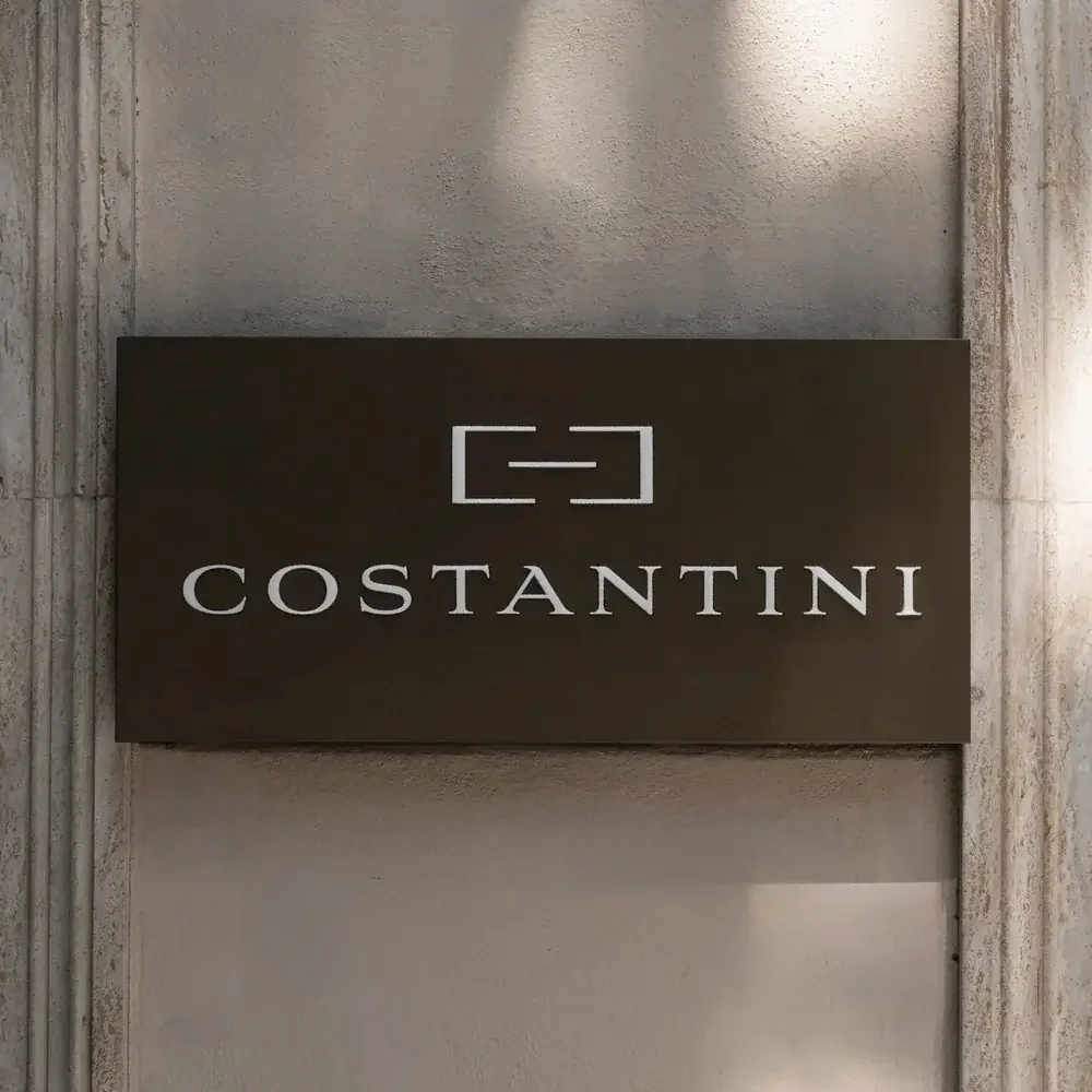 Signboard with the brand name "Costantini" and a logo above it, mounted on a concrete wall.