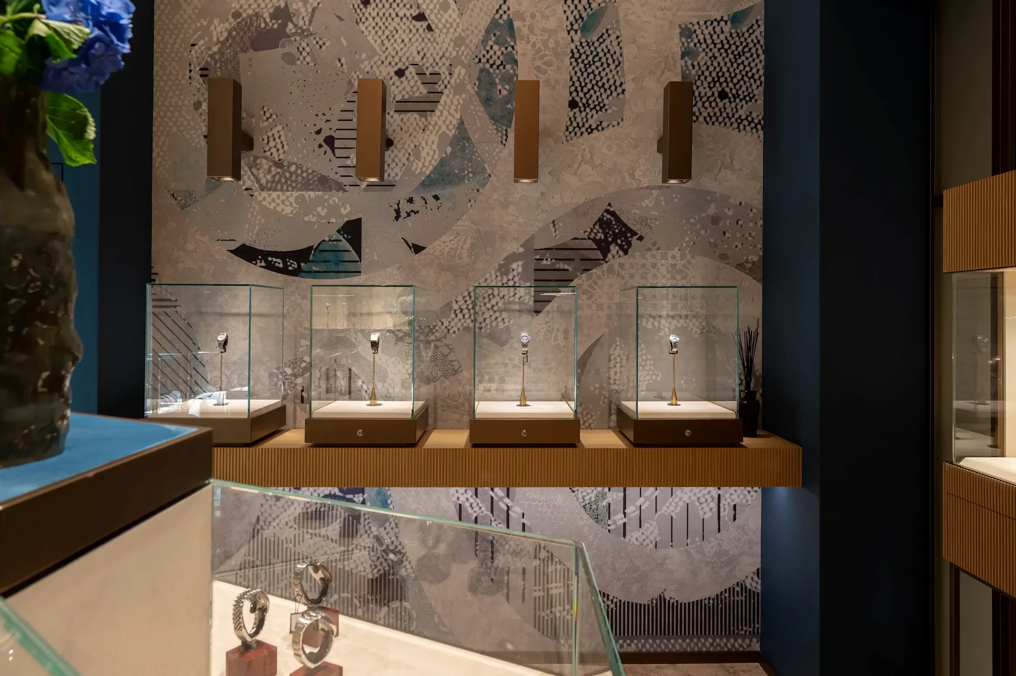 Jewelry display case with rings on stands in a luxury store, decorated with a geometric patterned wall behind.