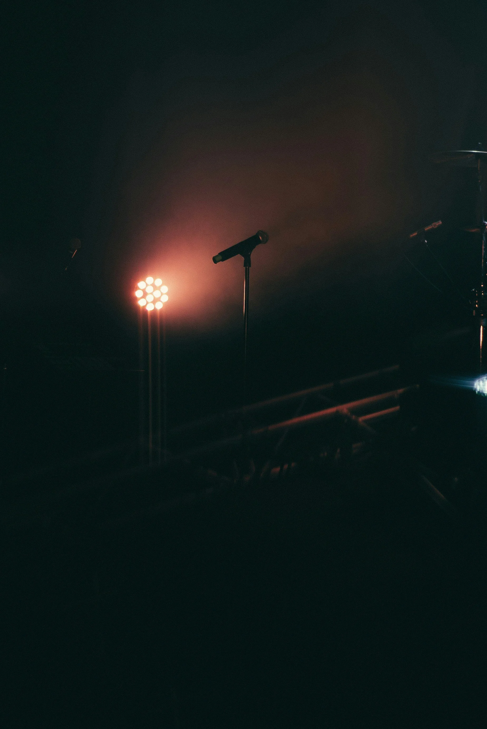 A stage with a microphone stand, bright stage lights, and musical instruments in the background, ready for a performance.