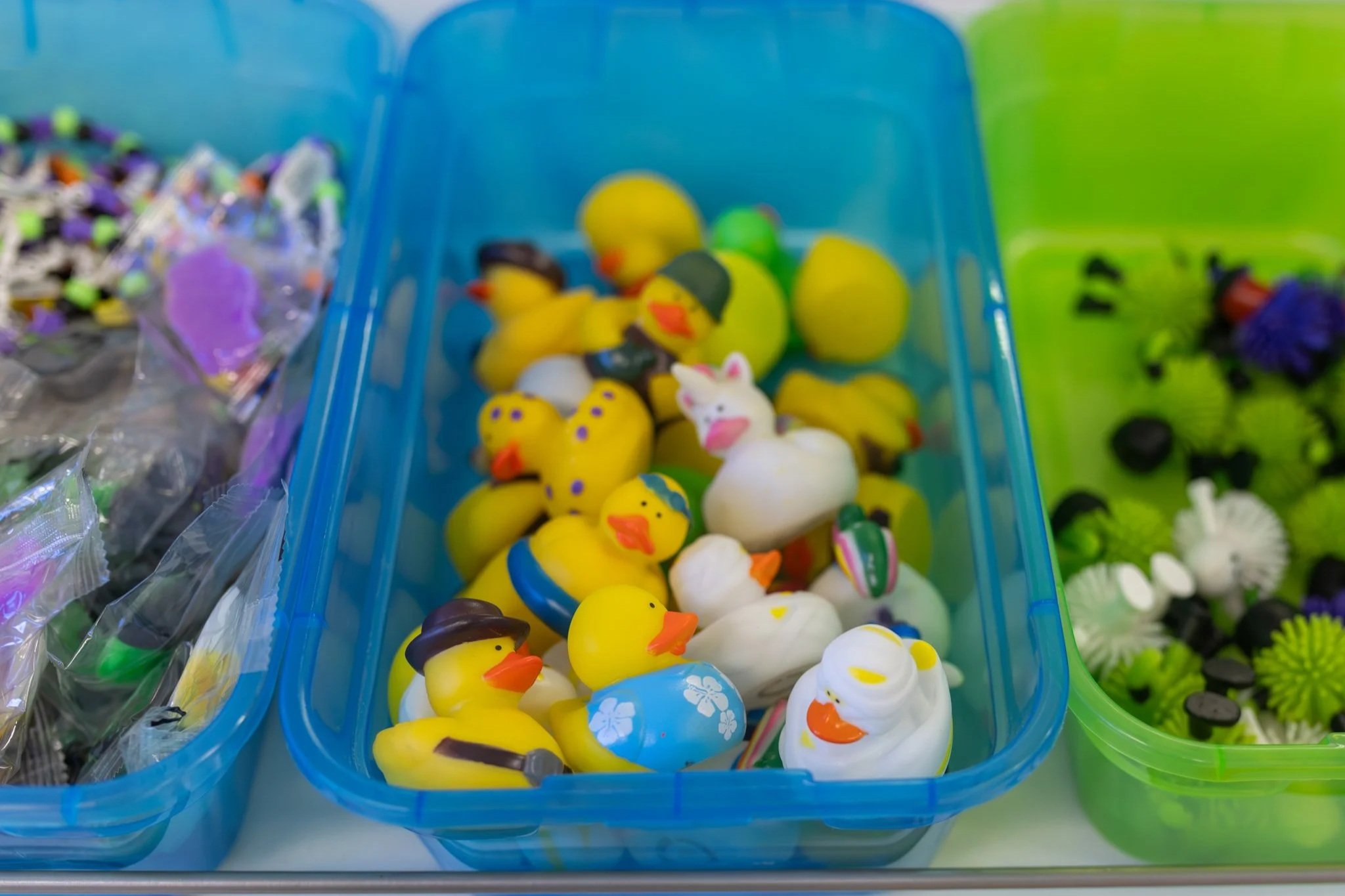 Plastic Easter chicks and ducks in a blue container, with some wearing accessories and others decorated with colorful patterns.