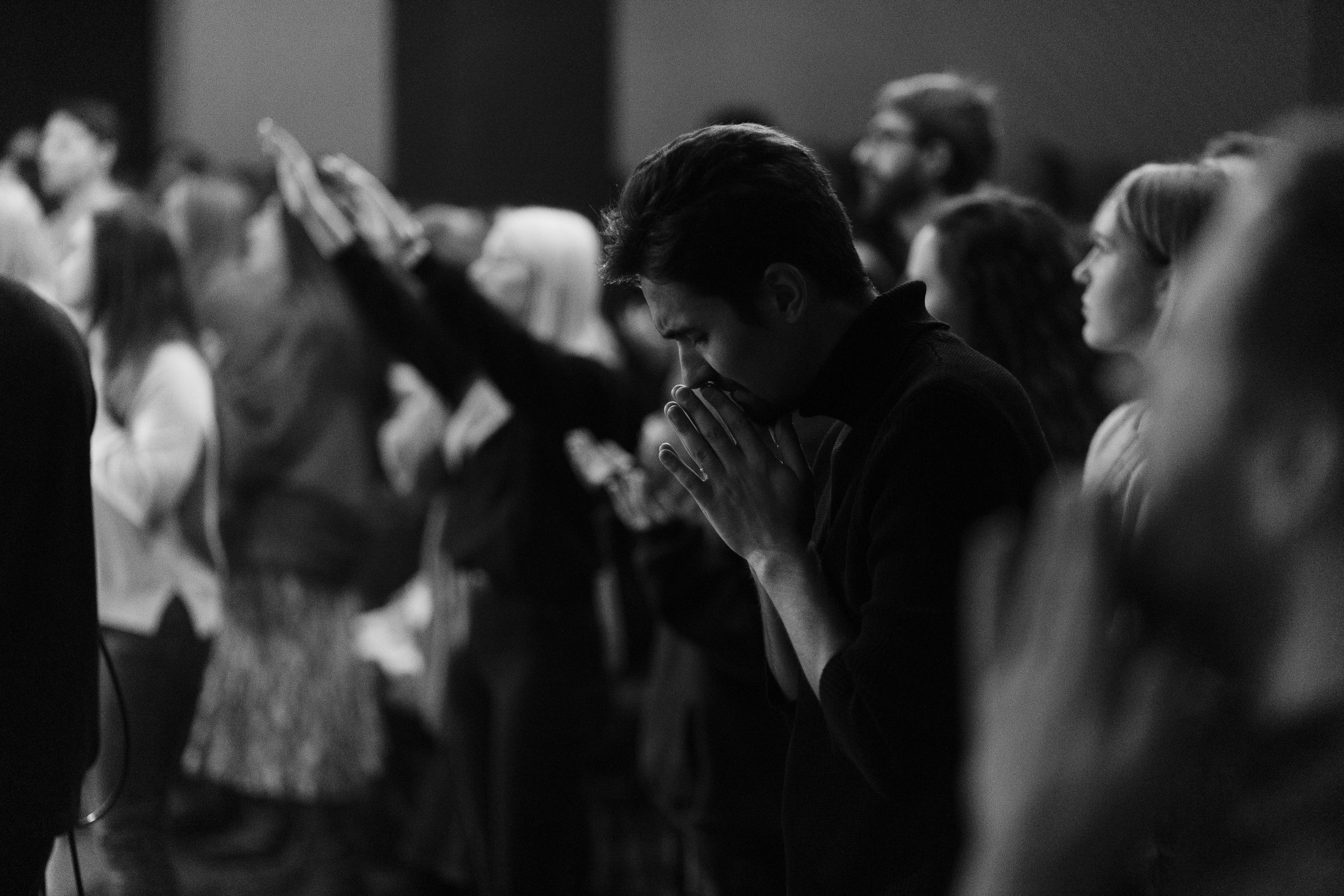 A group of people praying with hands clasped together in a church or worship setting, black and white photo.