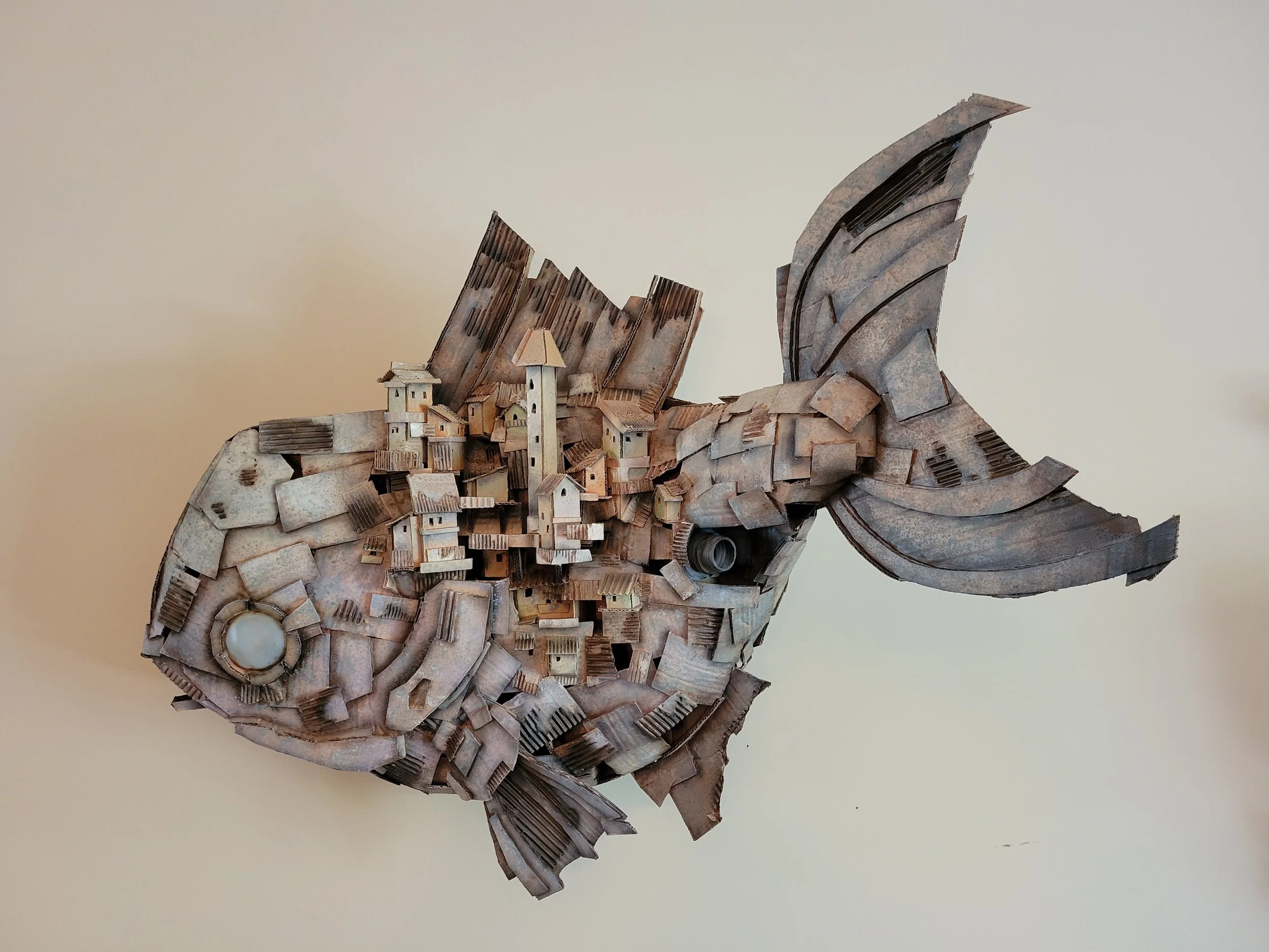 A sculpture of a fish made from cardboard and miniature houses.