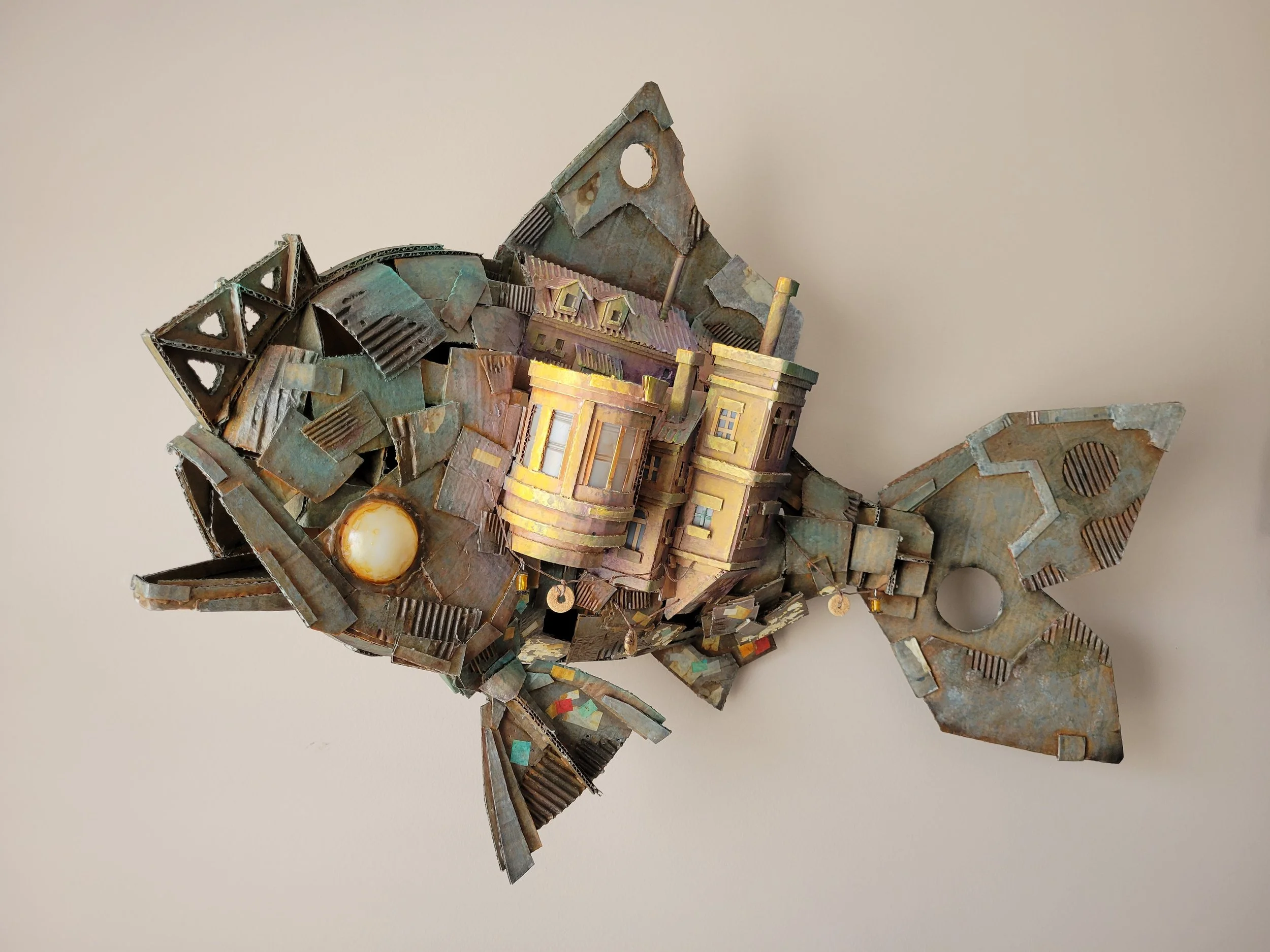 A sculpture of a fish made from cardboard with buildings attached.