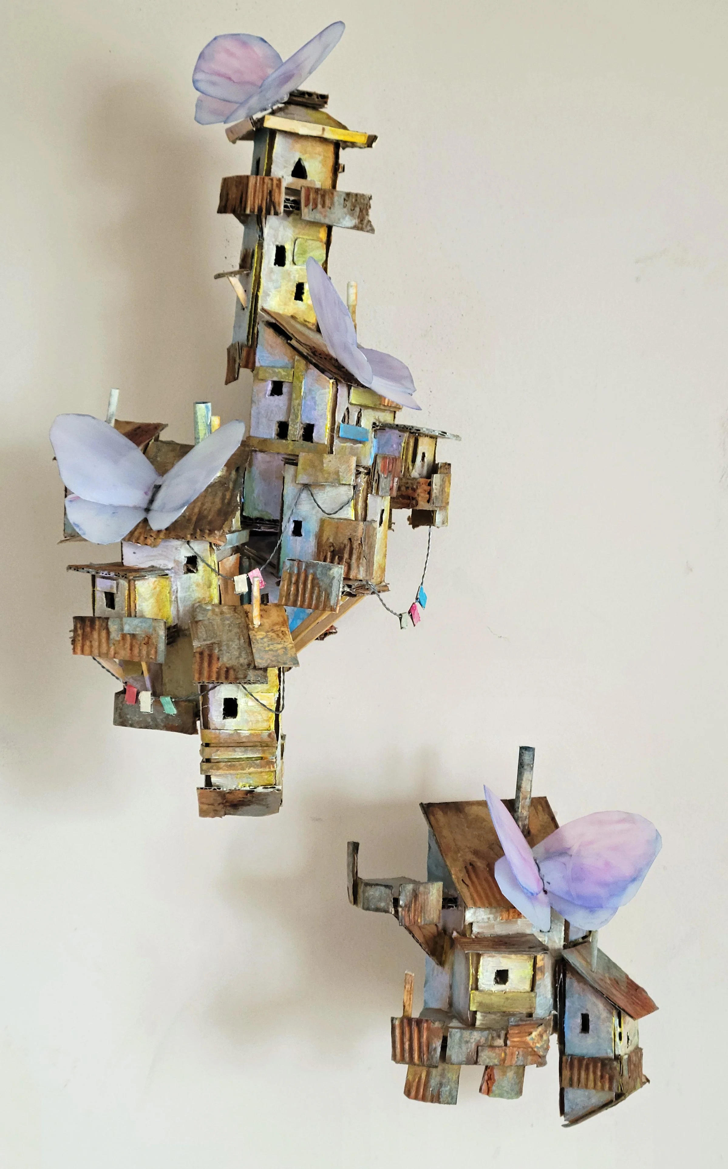 A handcrafted miniature village with small houses made from cardboard, decorated with pastel-colored butterfly  ornaments.
