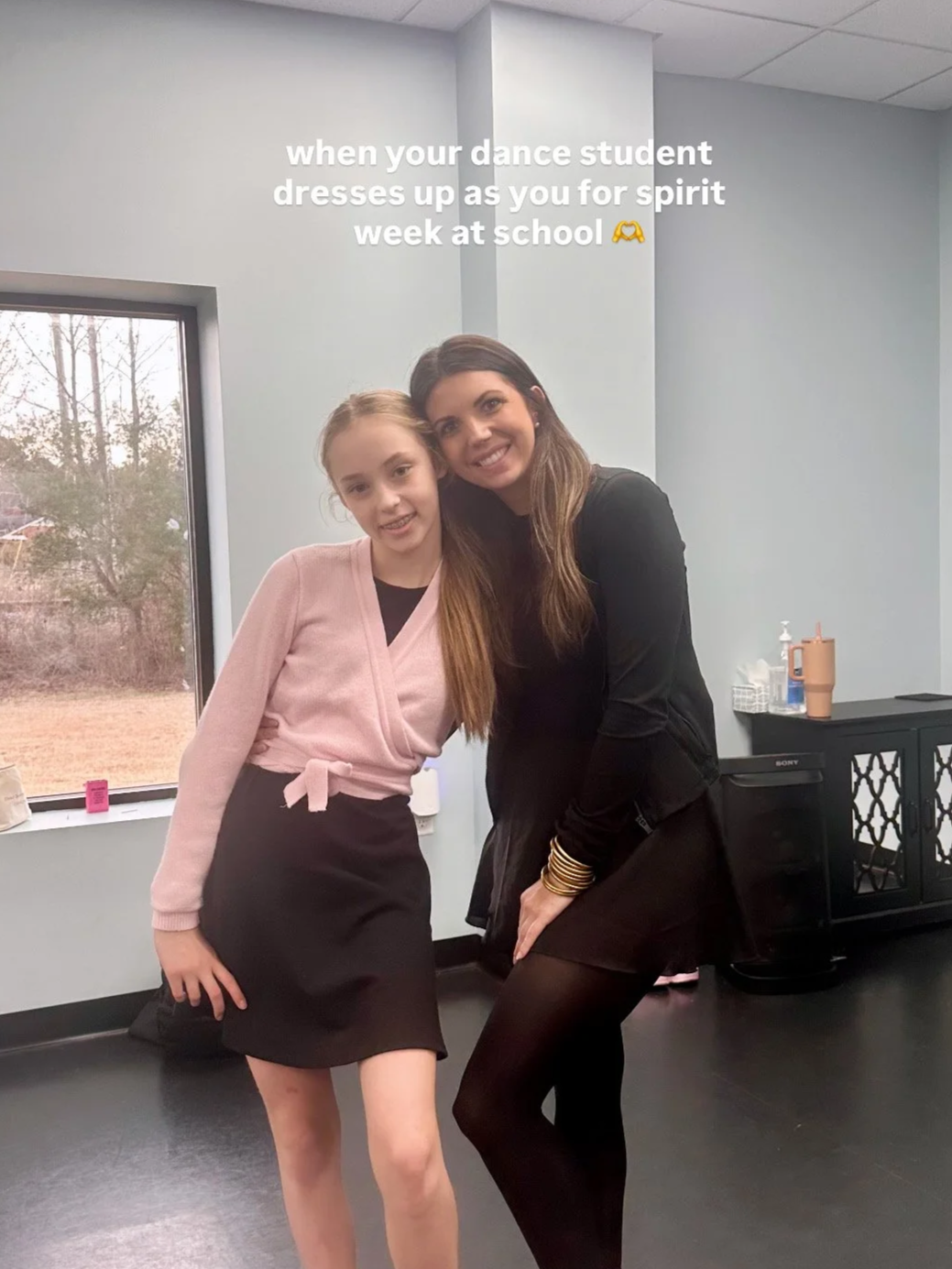 A young girl and an adult woman dressed in black, both smiling and posing together indoors, celebrating Spirit Week at school.