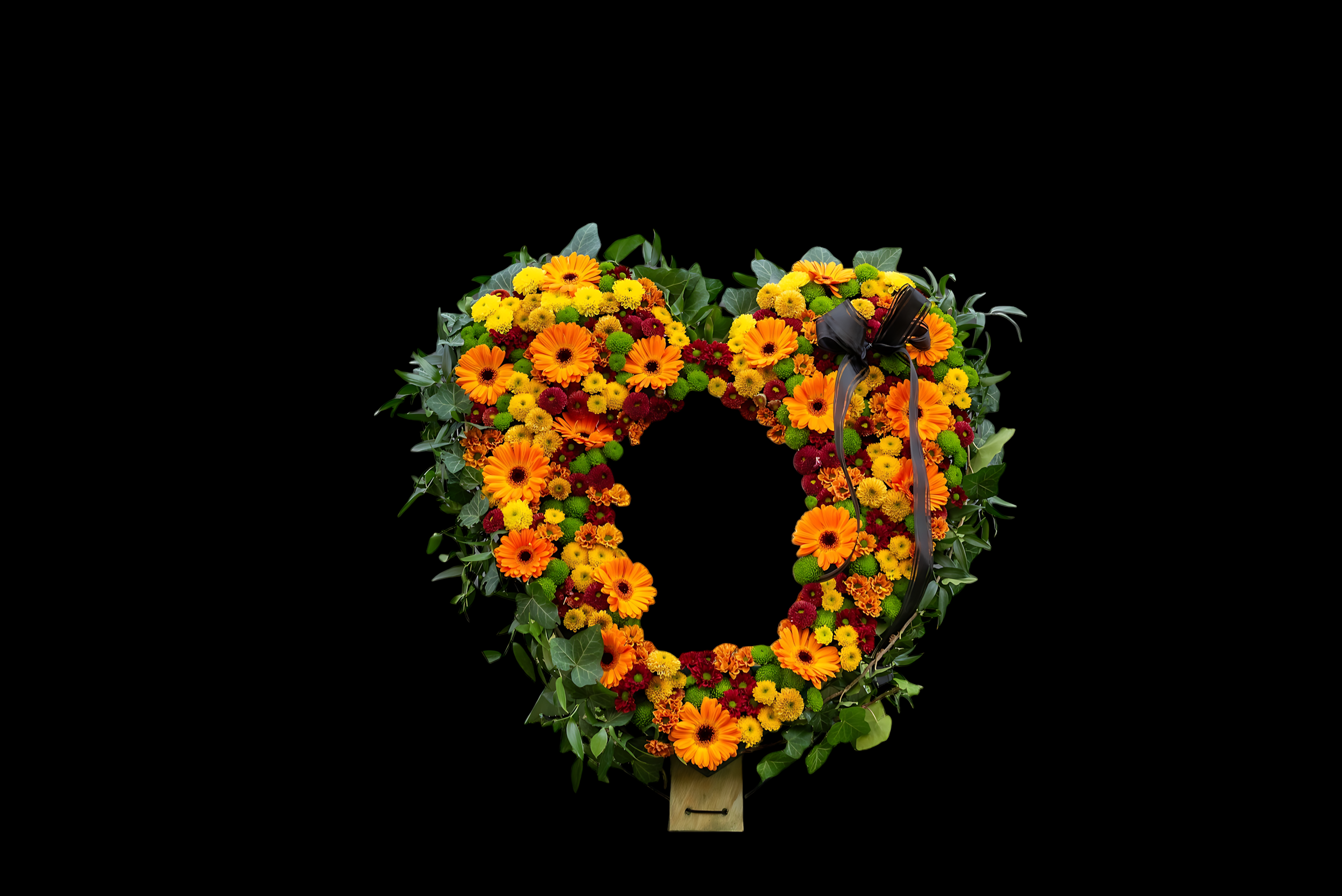 A colorful funeral wreath made of orange, yellow, and red flowers with green leaves, adorned with a black ribbon and photo memorial.