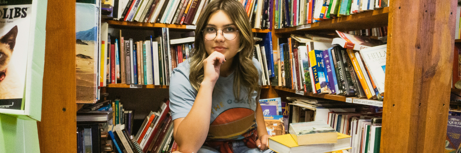 Teenage girl sitting in front of a stack of books on a shelf