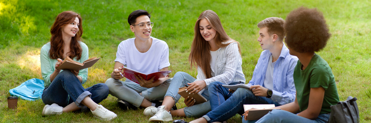 Group of teens sitting on the grass holding books.