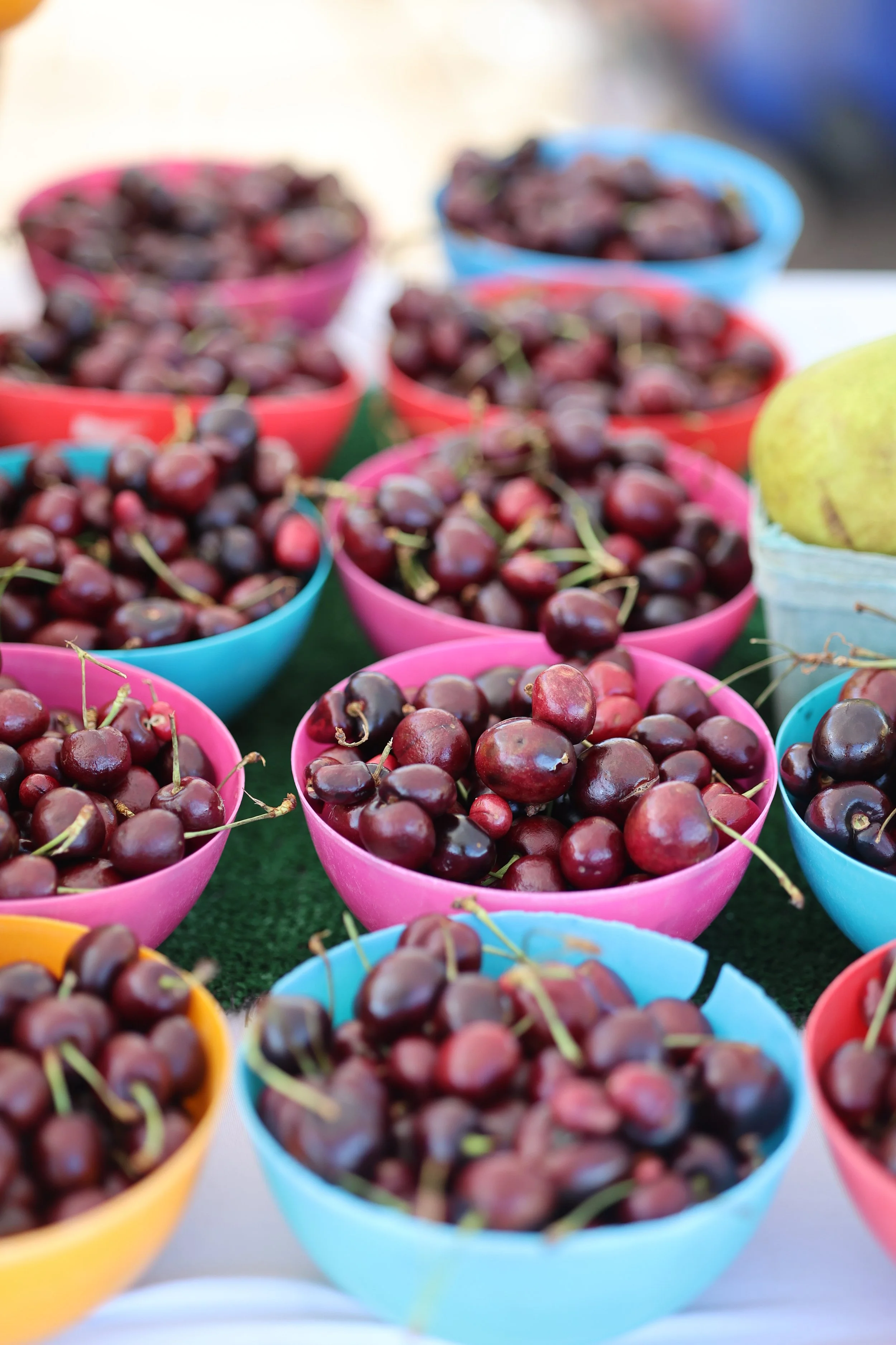 Multiple colorful bowls filled with red cherries.