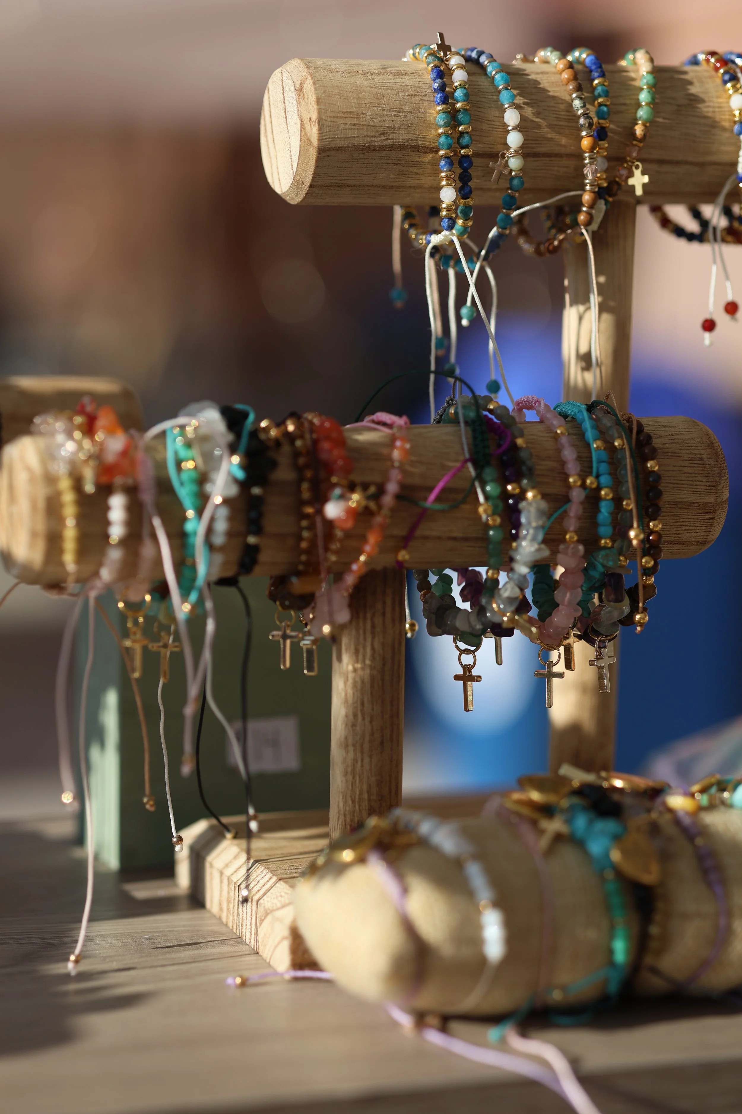 Display of colorful beaded bracelets with cross charms on wooden stands at a craft market.