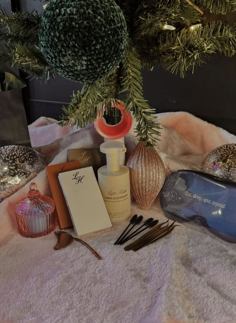 Christmas tree with ornaments and hygiene products on a soft pink surface.