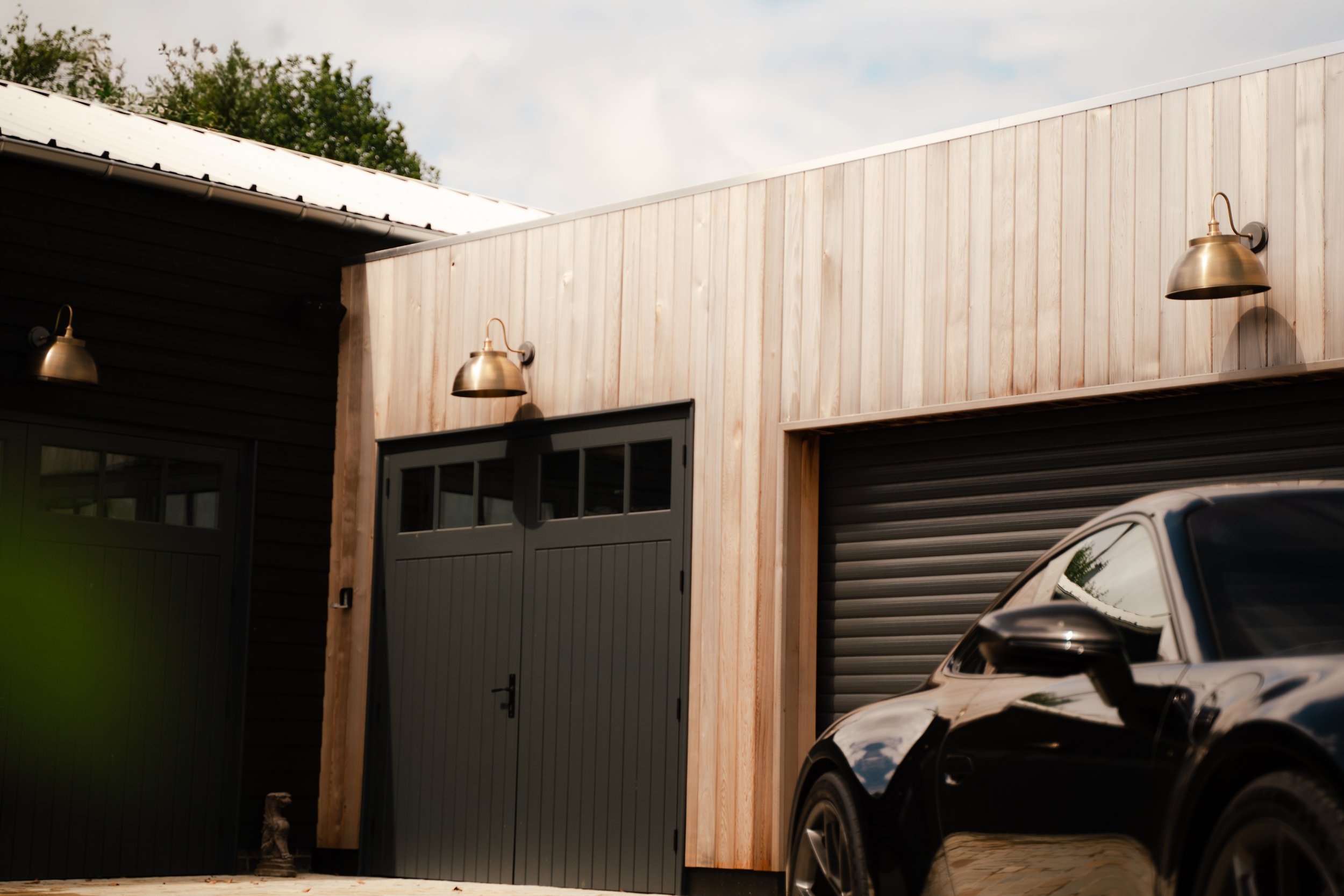 Exterior view of a modern building with black and light wooden siding, metallic wall sconces, a garage door, and a car parked in front.