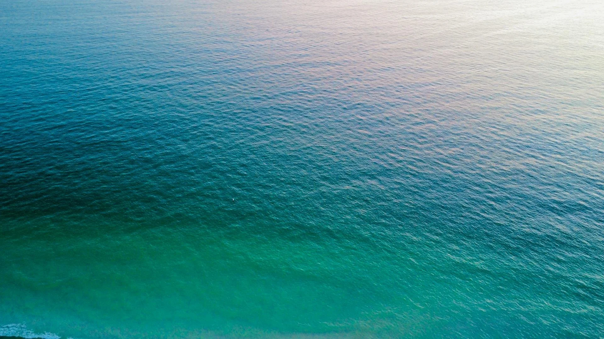 Aerial view of the ocean with blue and green water and gentle waves.