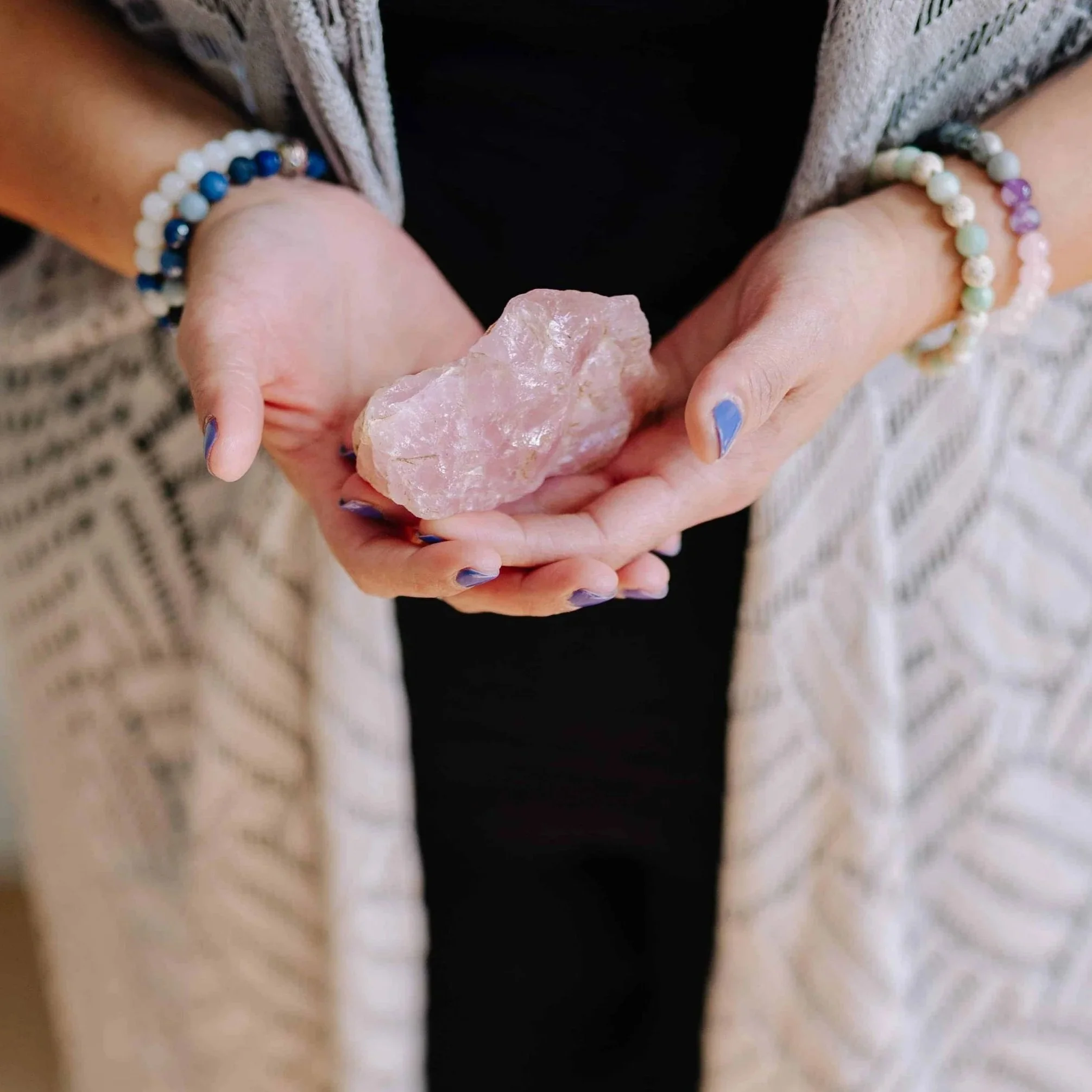 Person holding a large pink crystal with both hands, wearing colorful beaded bracelets.
