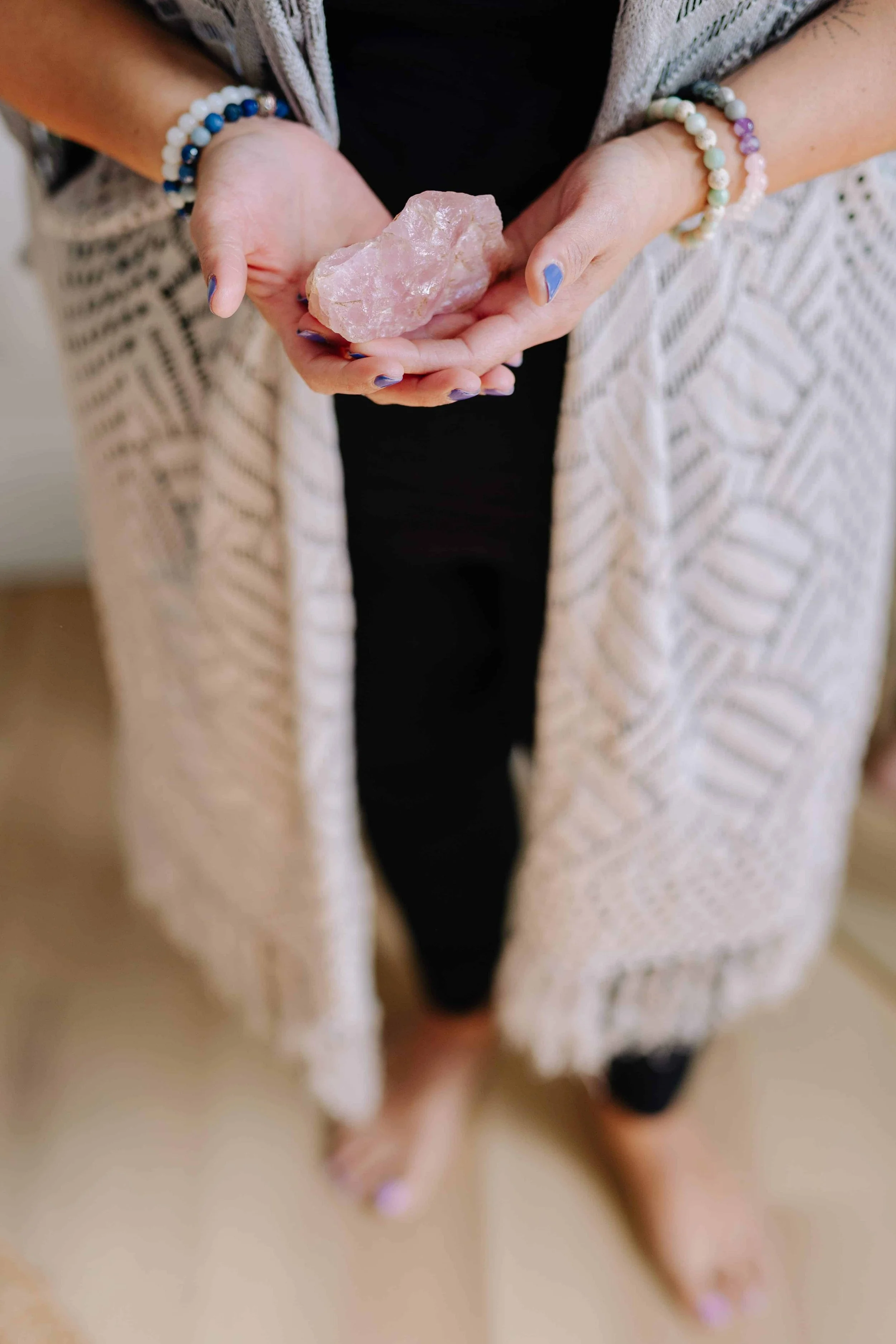 Woman in long beige sweater holding pink quartz rock in her hand in a welcoming way.