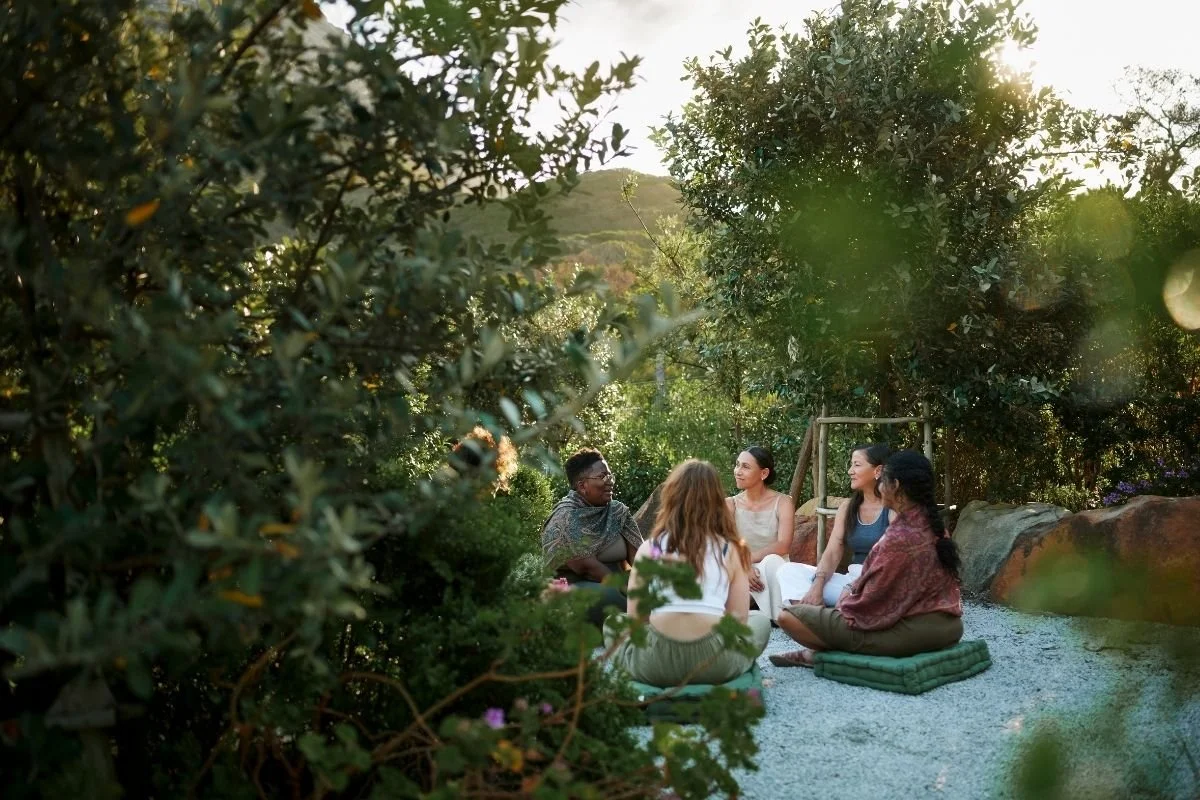 Group of women sitting in a circle outside at sunset in a large garden.