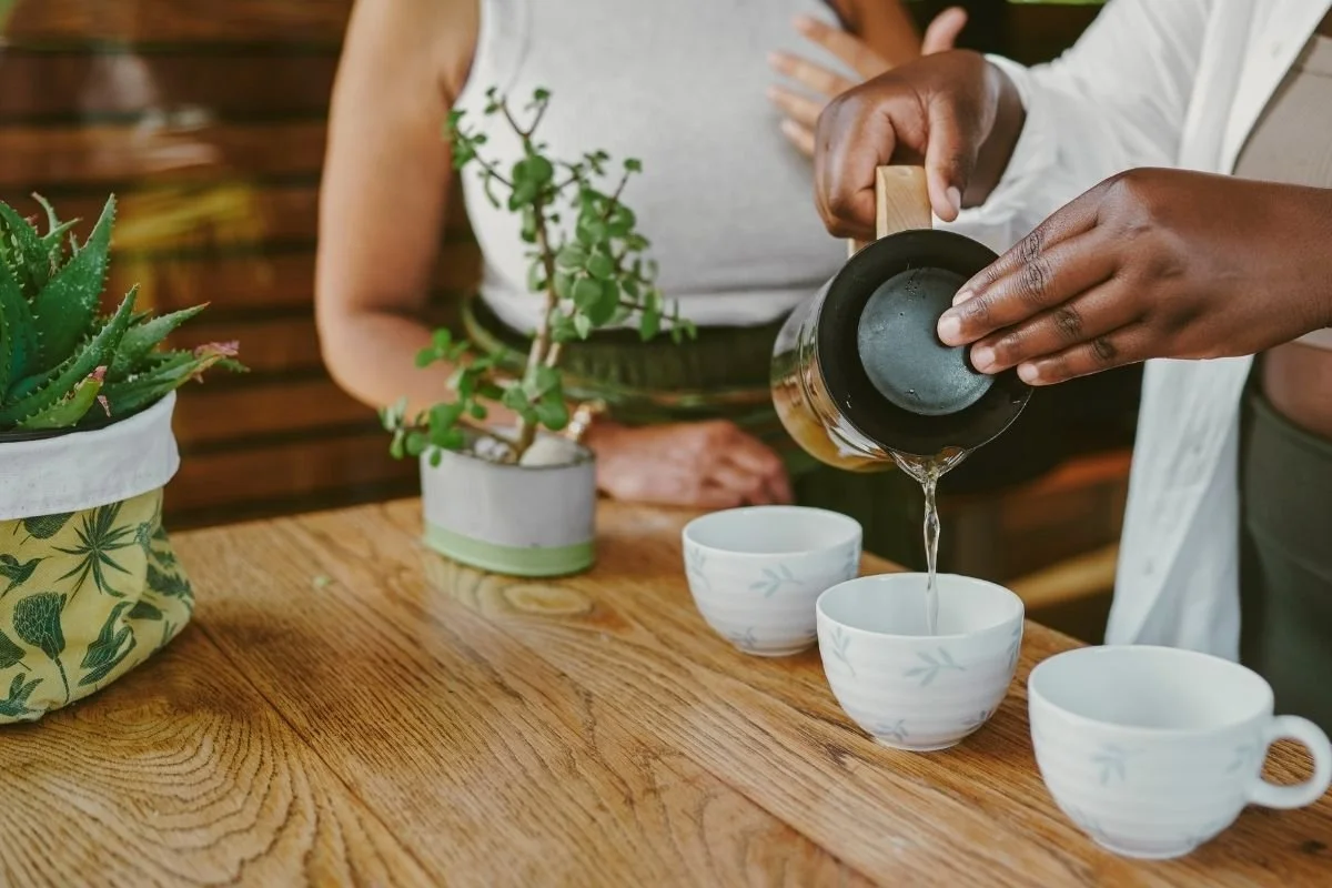 Image of tea being poured into small white tea cups on a wooden table.