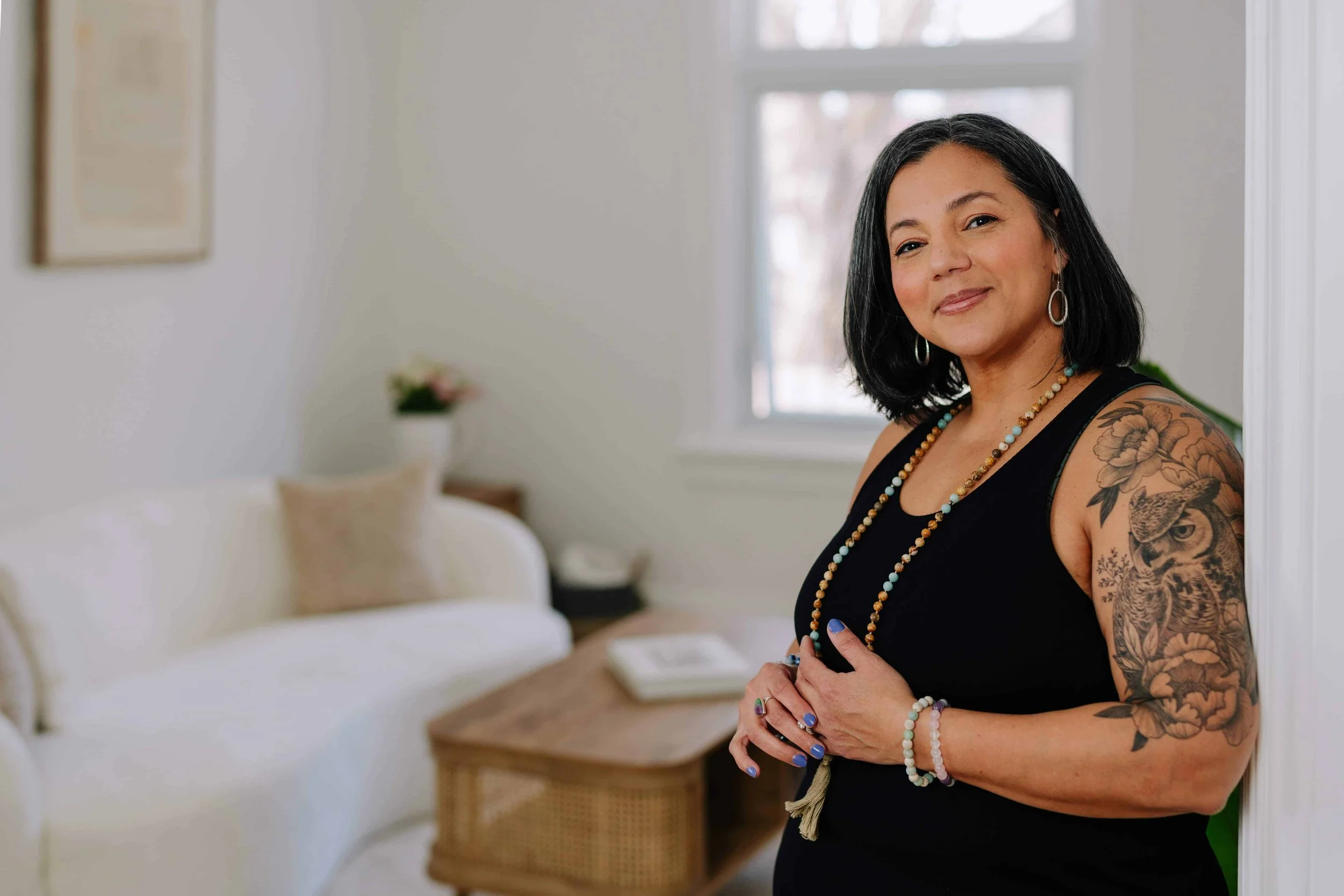 Woman in black tank top smiling warmly wearing a long beaded necklace and purple nail polish.