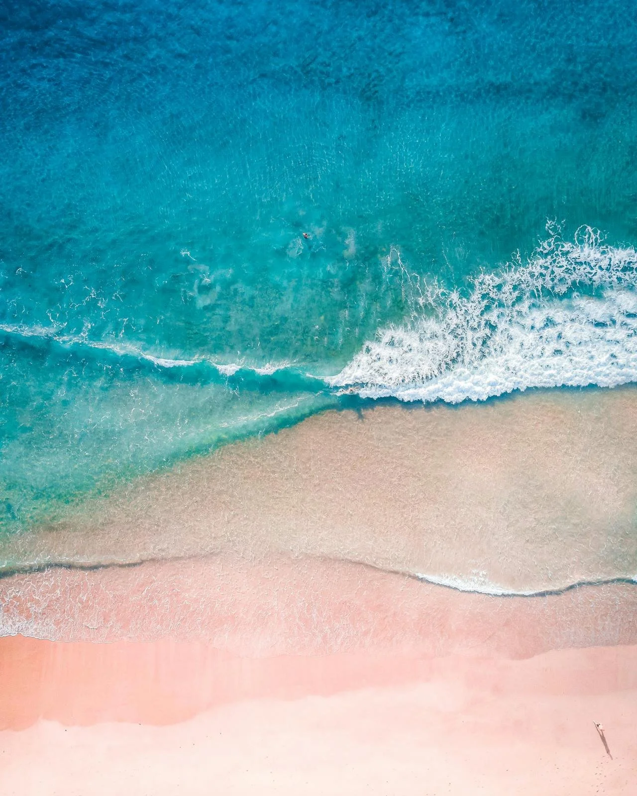 Turquoise and teal water with waves falling onto sandy beach.