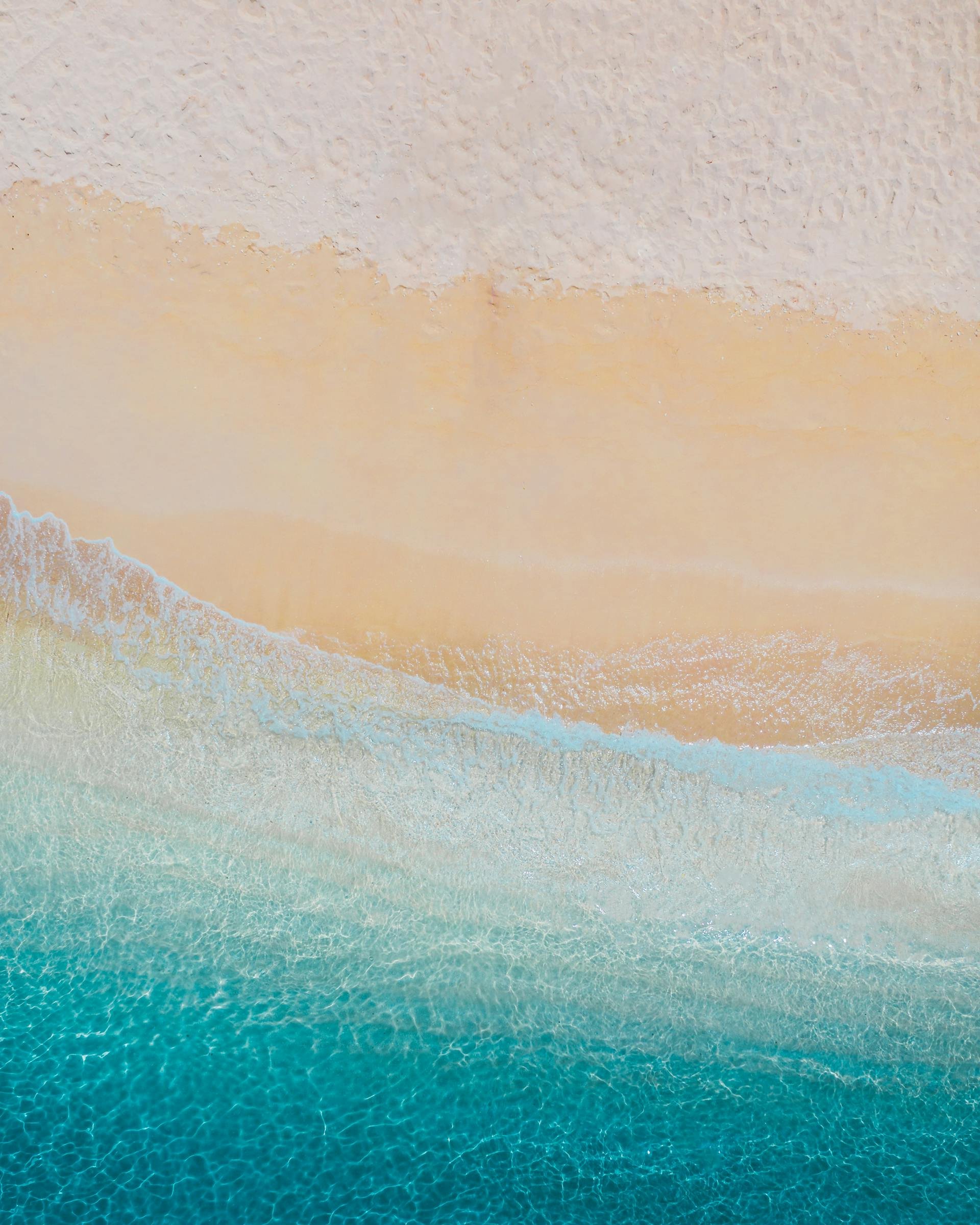 Aerial view of a beach with sand meeting the turquoise ocean water.