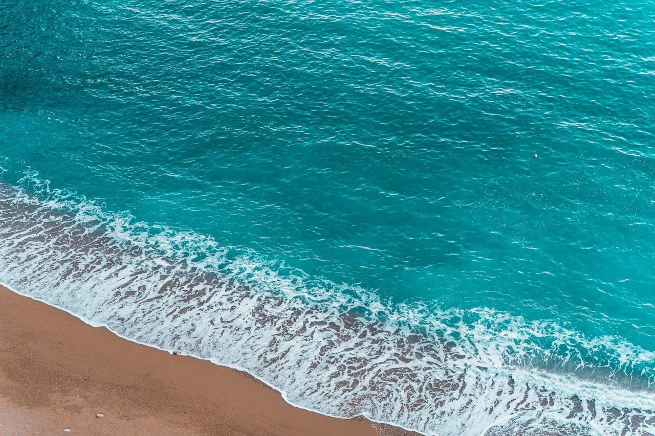 Teal ocean wave breaking on the sandy shoreline.
