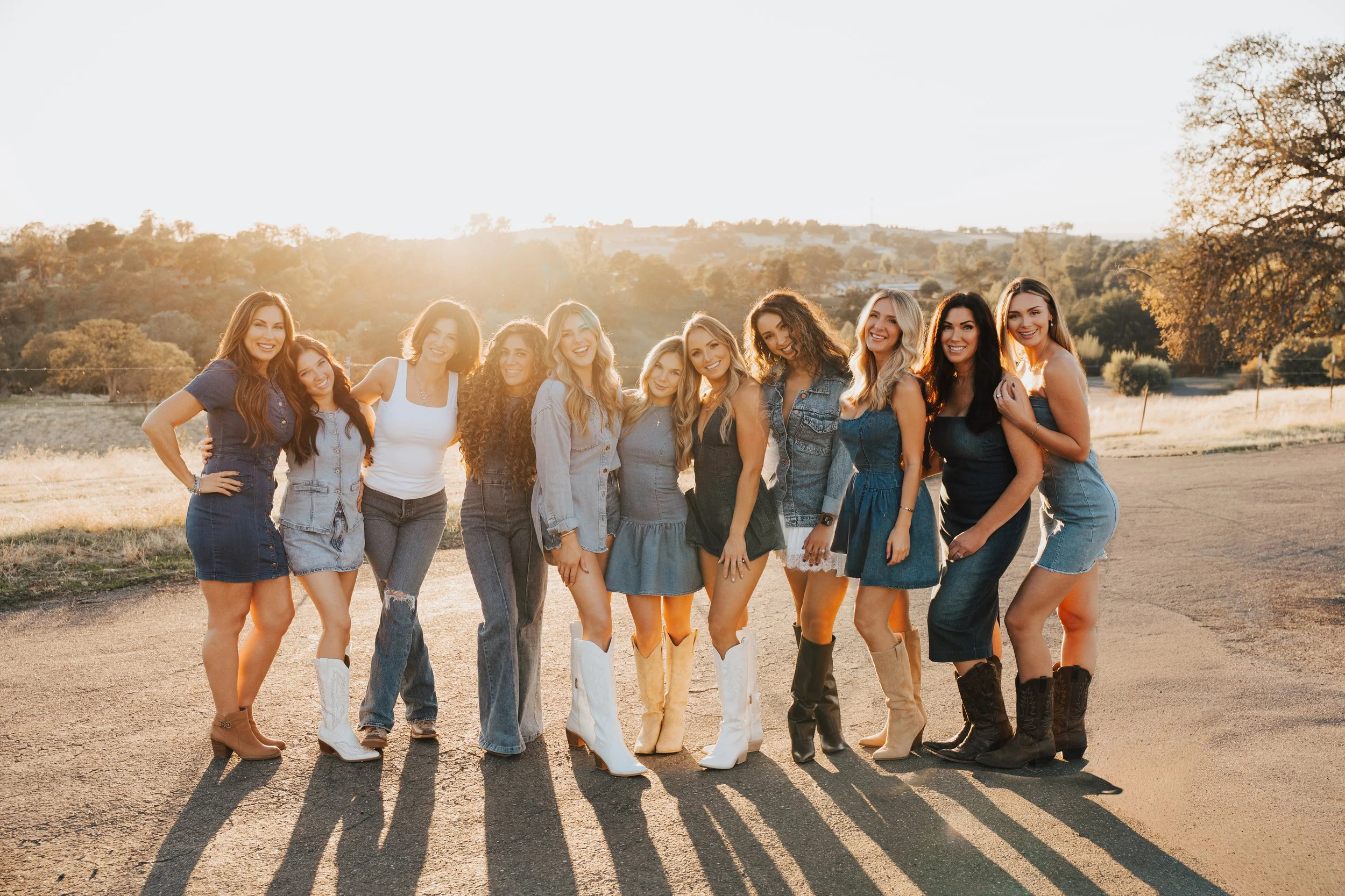 Group of eleven women standing outdoors in a row, smiling, during sunset.