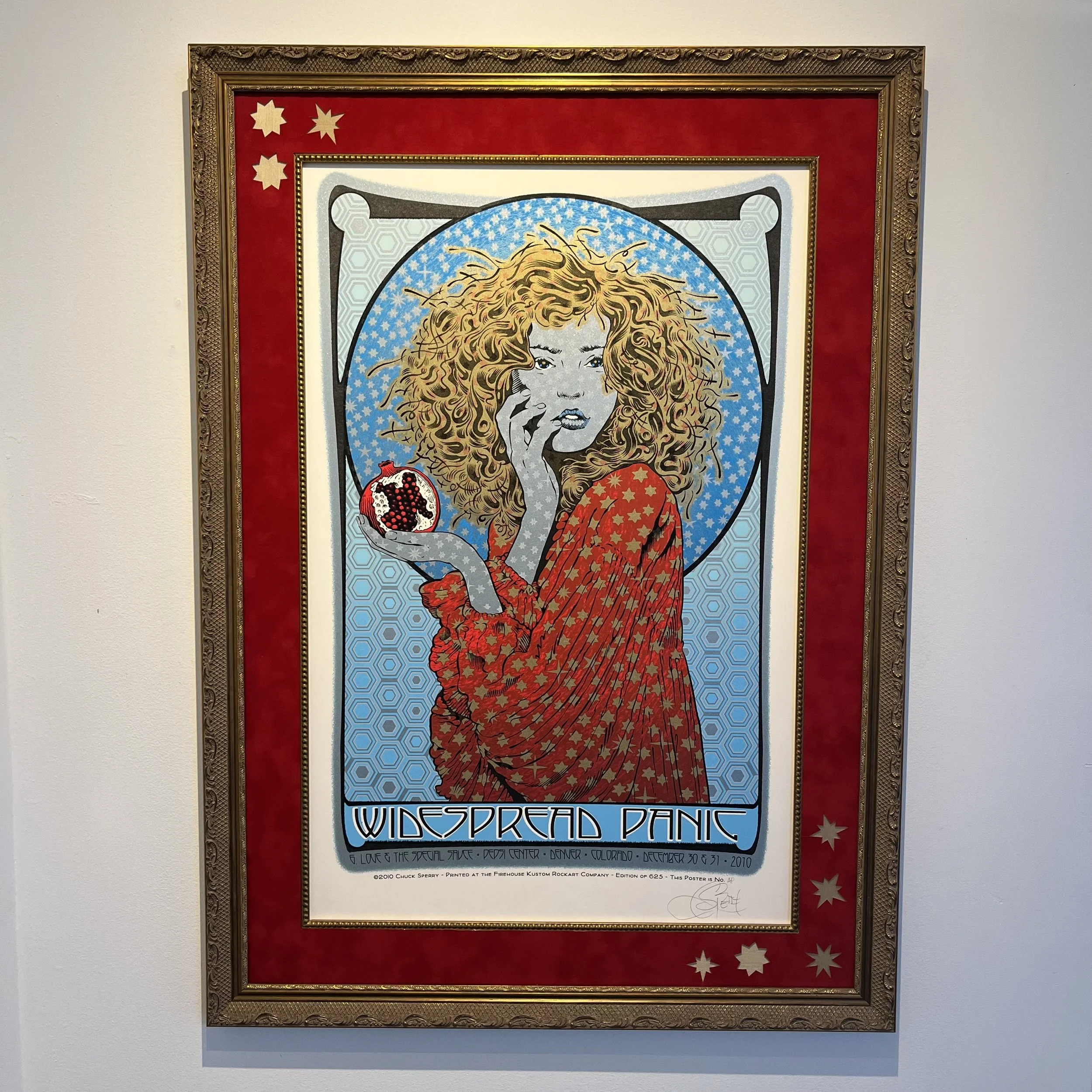 Colorful artwork featuring a woman with curly red hair, holding an apple in one hand, with a blue and white circular background and a red border with stars, titled 'Widespread Panic'.