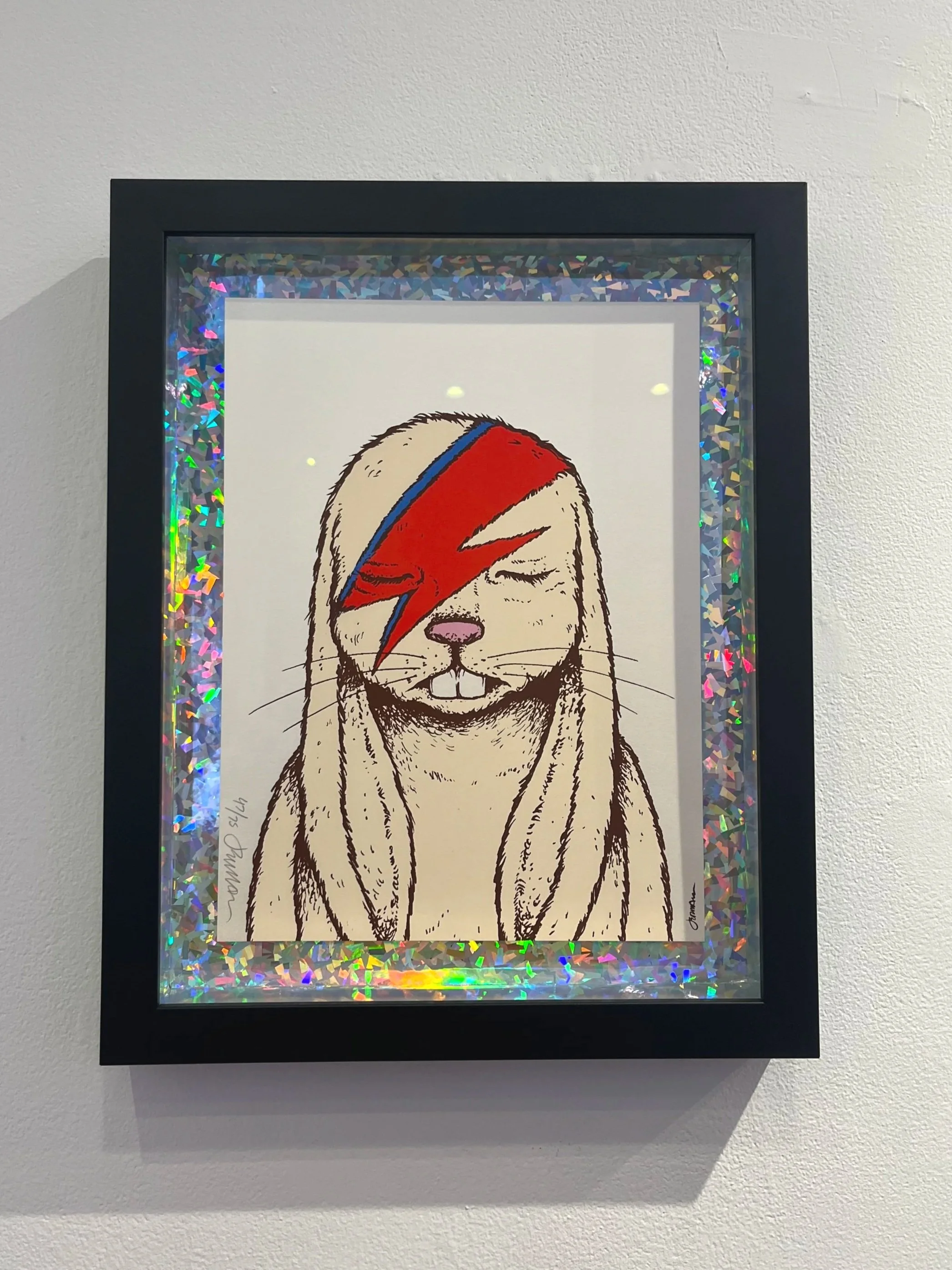 Framed artwork of a cartoon rabbit with long ears and a pink nose, wearing a red and blue lightning bolt face paint, with a holographic border.