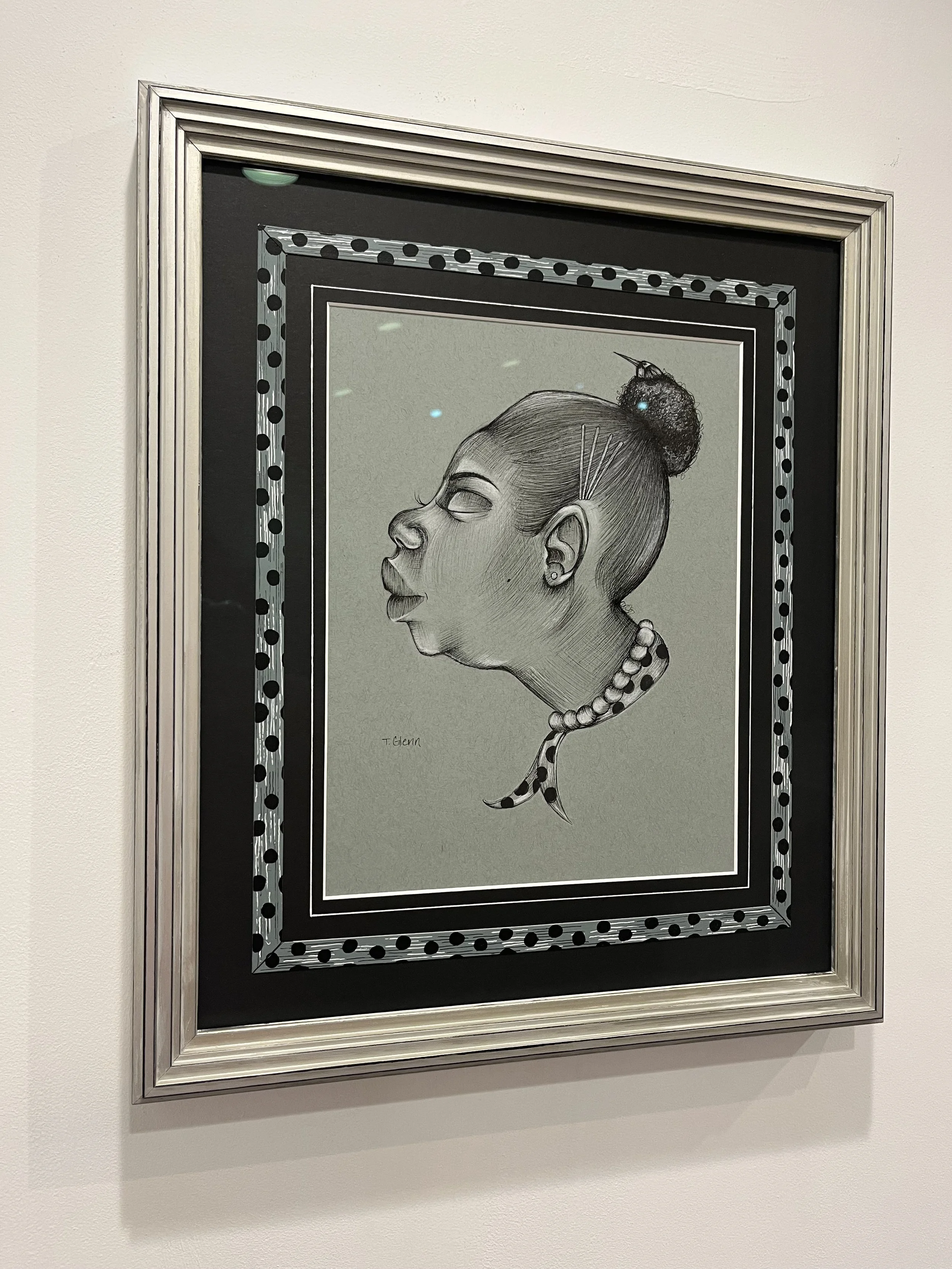 A black and white portrait of a woman with her hair in a bun, wearing pearl earrings and a pearl necklace, with a bird perched on her head.